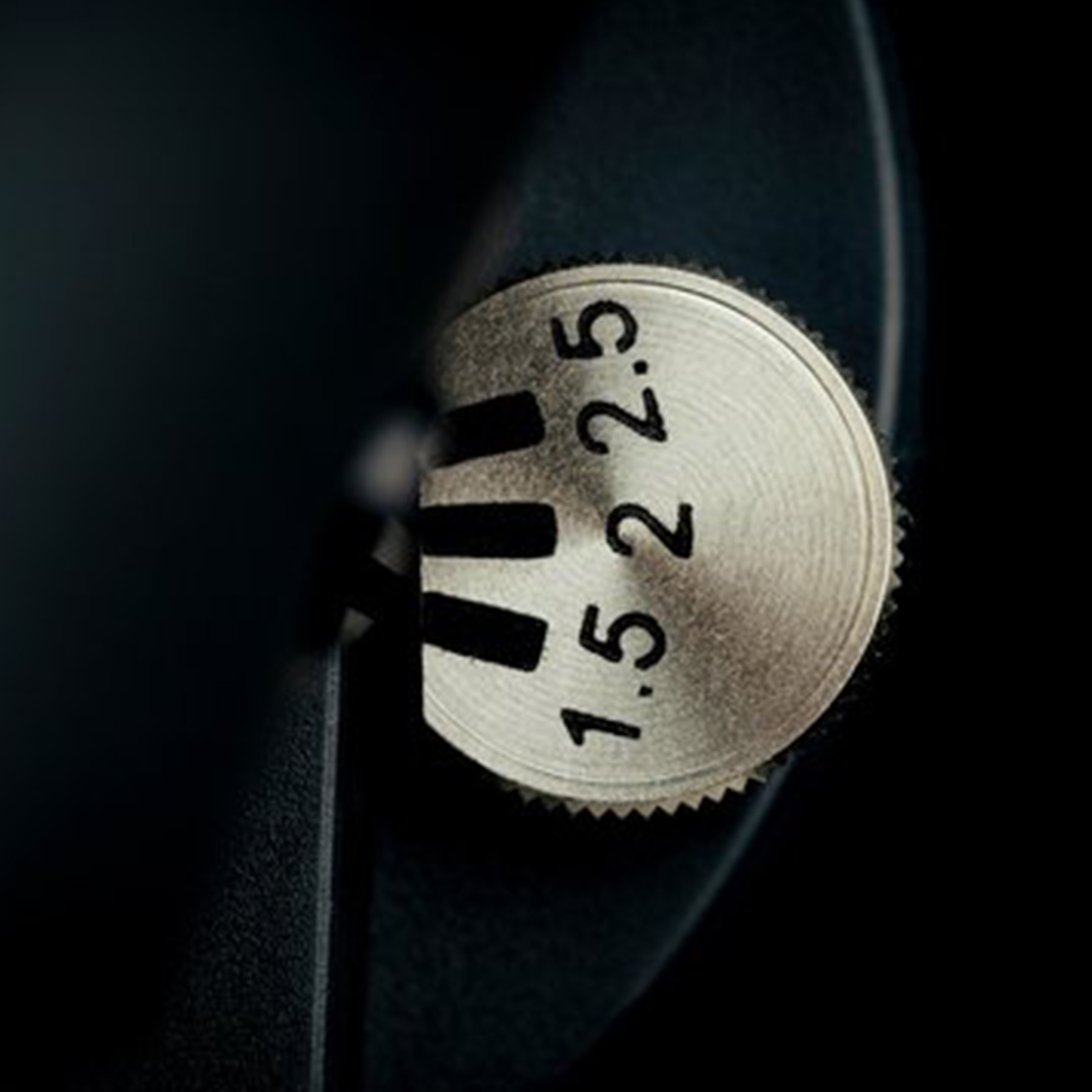 A close-up of a silver dial with numbers and markings, set against a dark background, with focus on 1.5 and 2.5.