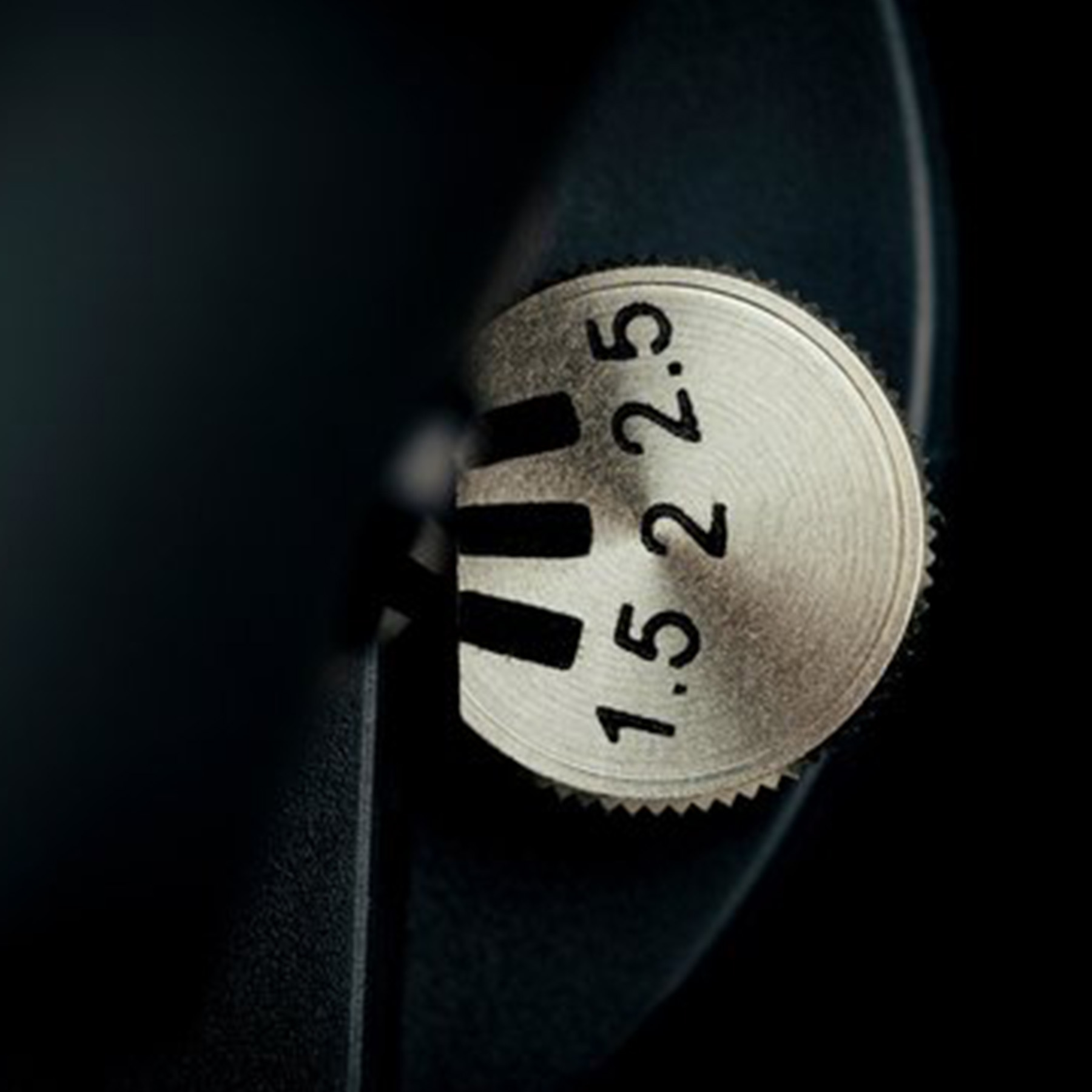 Close up of a metallic dial with numbers. Black surface in background.