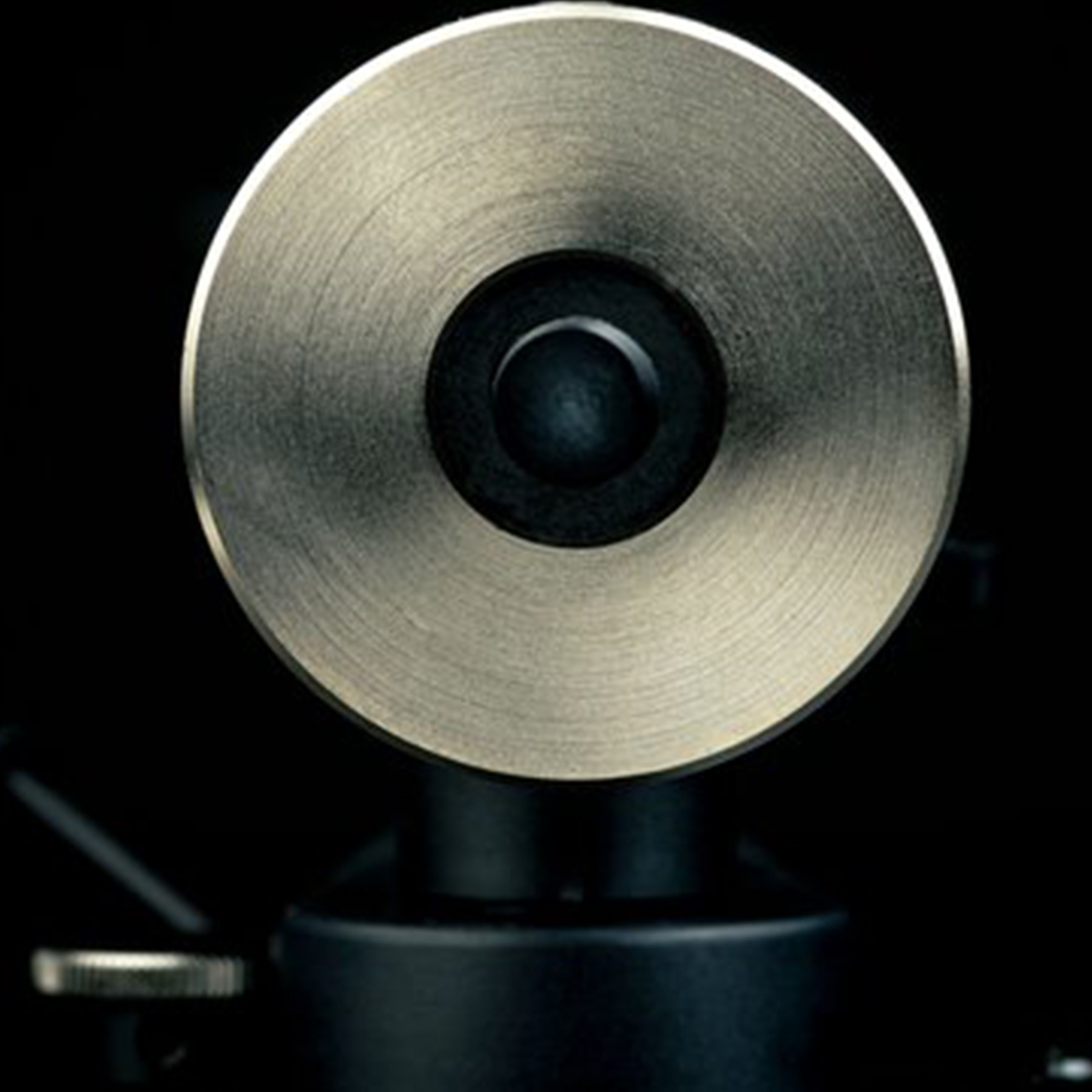 Close-up of a gold-colored speaker component with a central black hole on a black background.