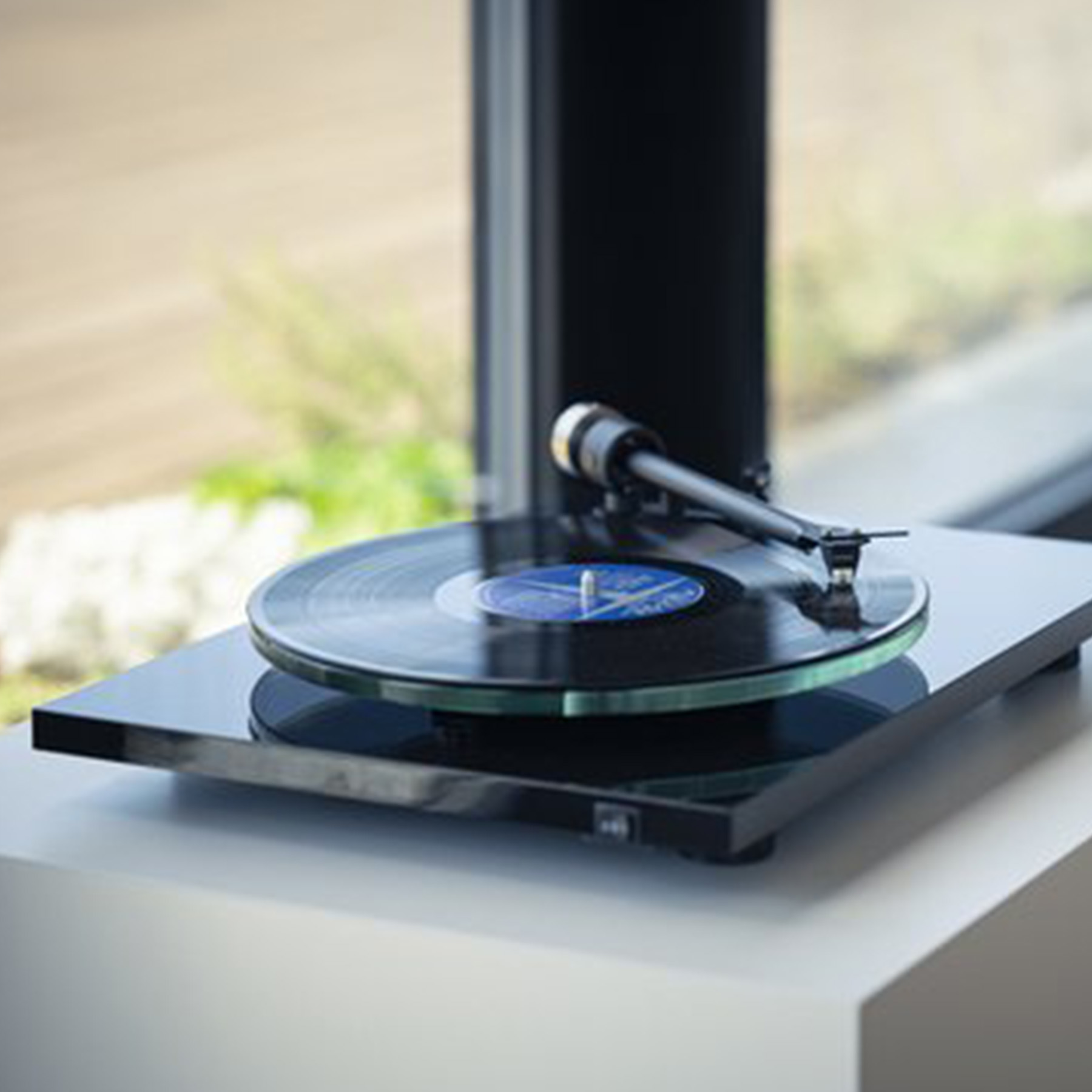 A turntable with a black base and a vinyl record playing, set on a white surface.