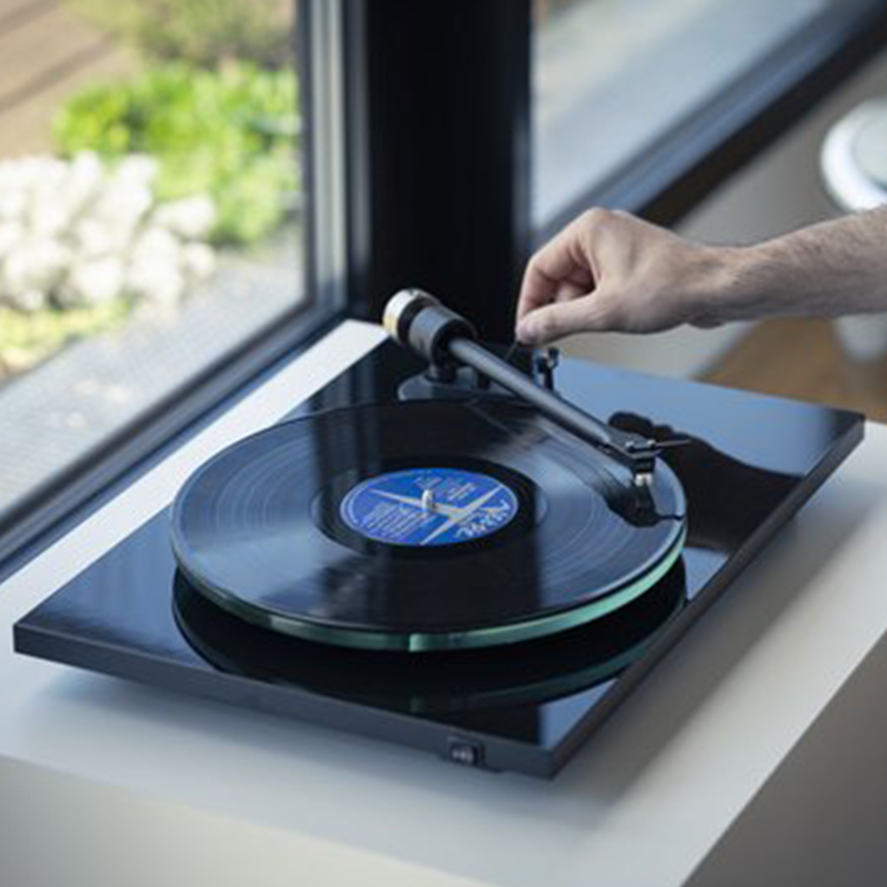 A person's hand adjusting a record player's arm, with a record on it.