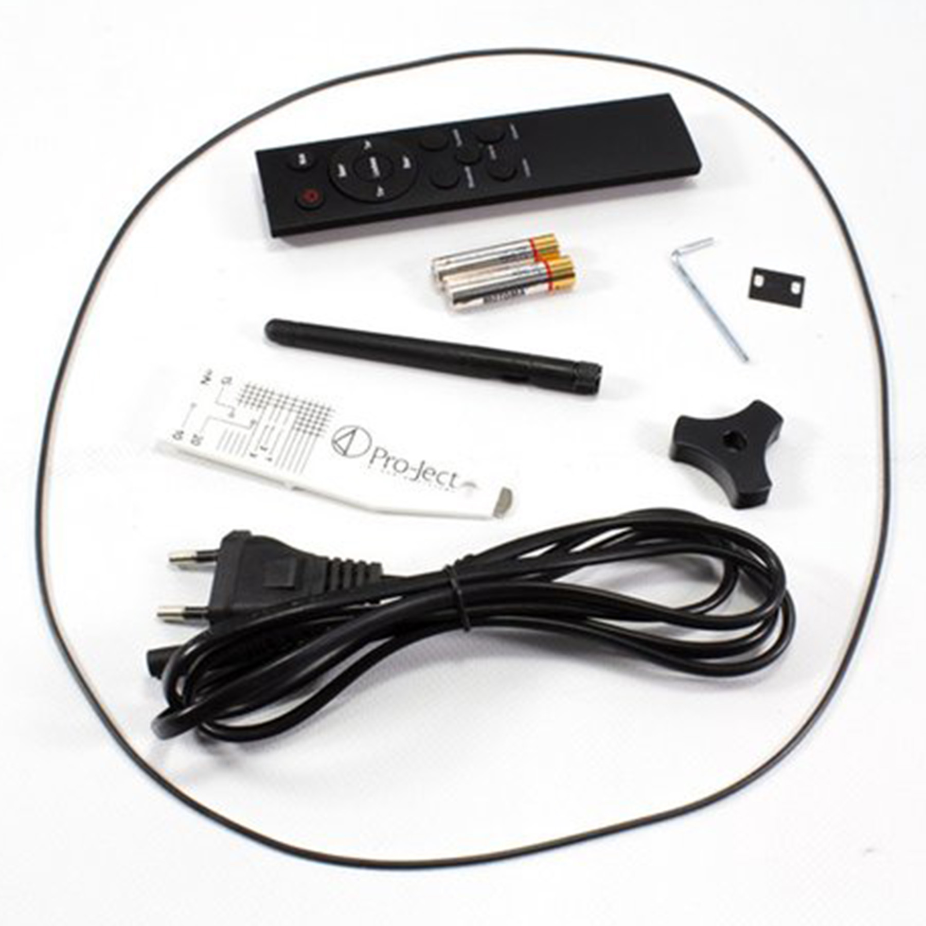 Akcesoria do gramofonu na białej powierzchni. Zawiera pilota, baterie, kable i szczotkę.