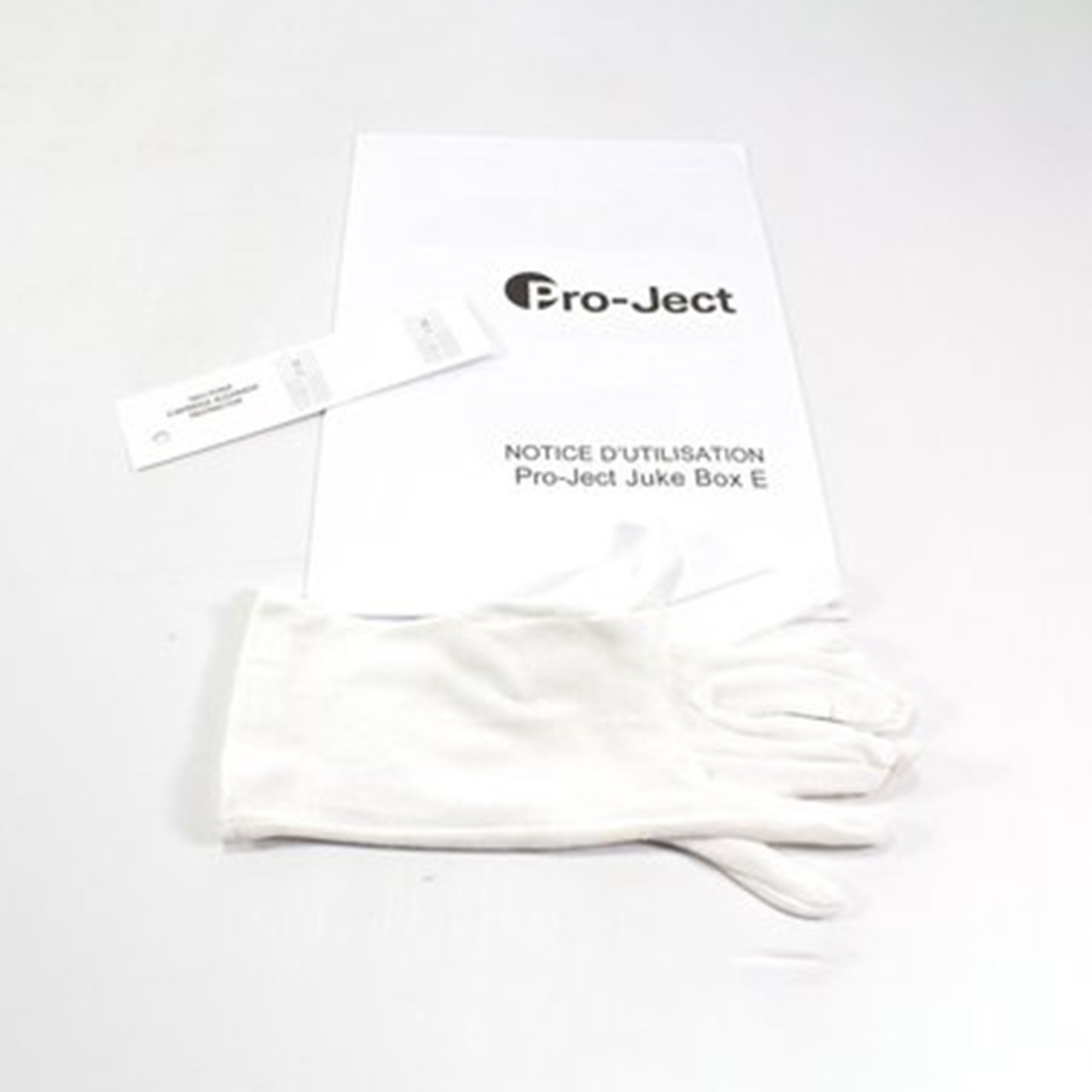 Białe rękawice, instrukcja Pro-Ject i mały papier gwarancyjny, ułożone na białej powierzchni.