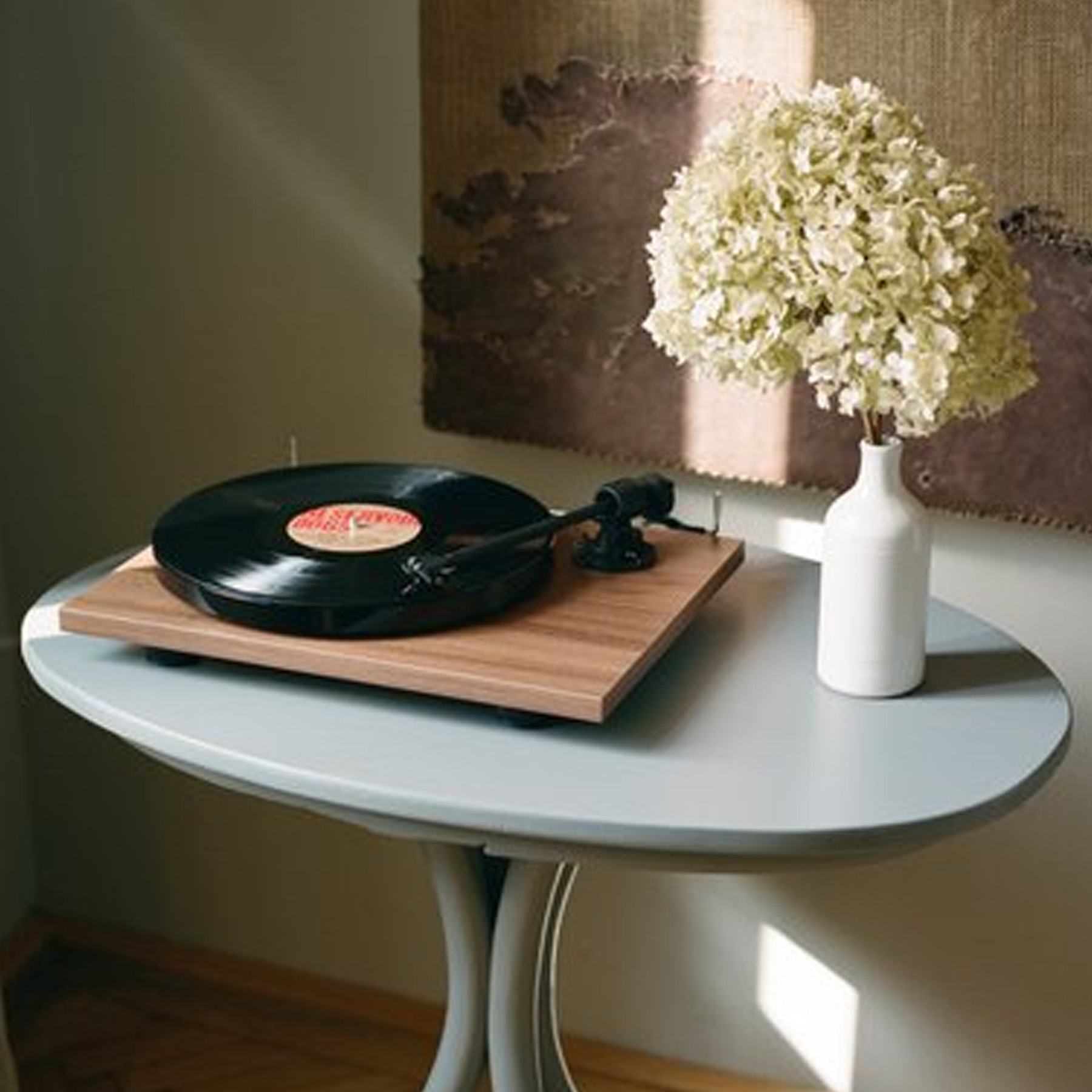 Plattenspieler auf hellblauem Tisch, mit Blumenvase rechts.