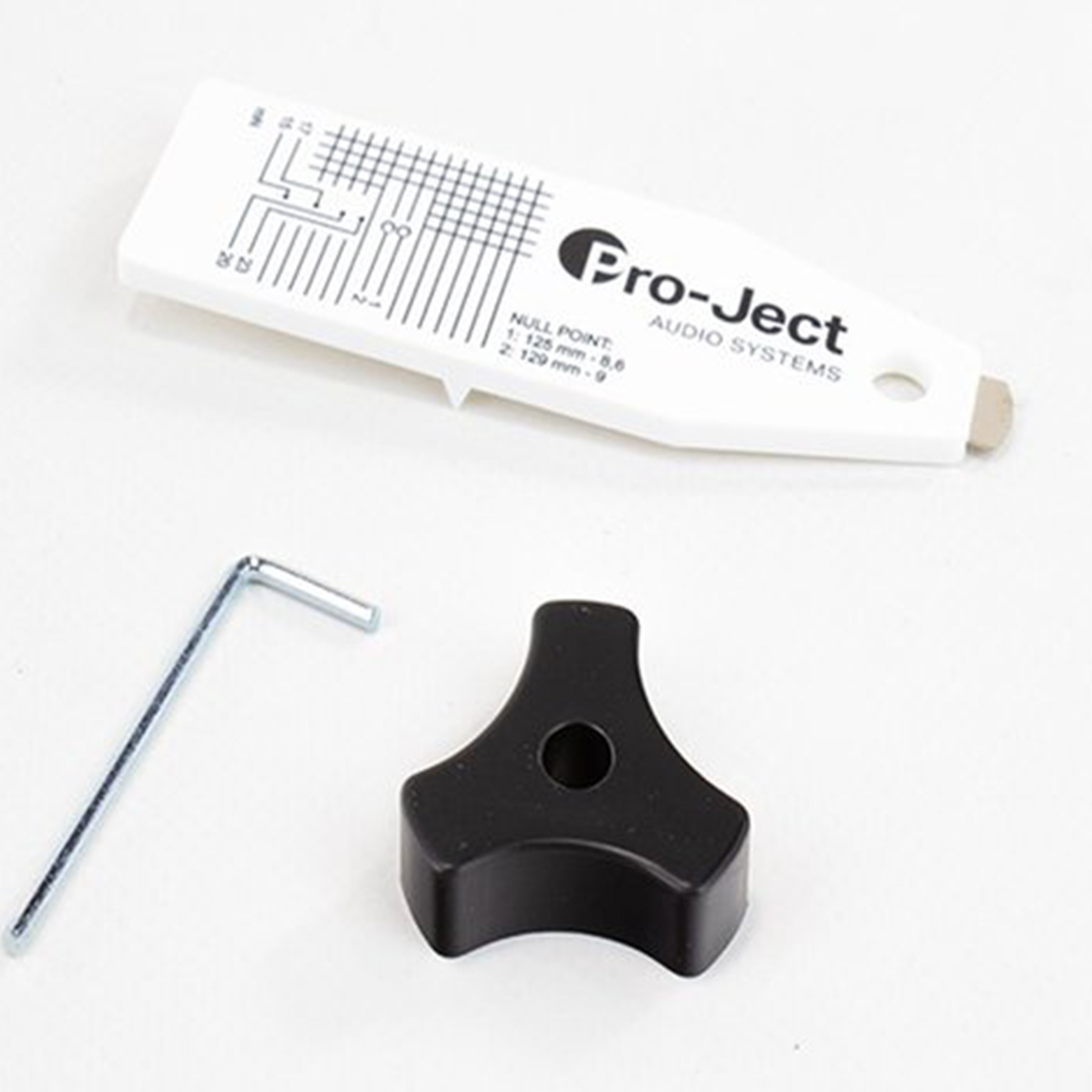 Weißer Stift, schwarzer Knopf und Schraubenschlüssel auf Weiß. Pro-Ject-Etikett.