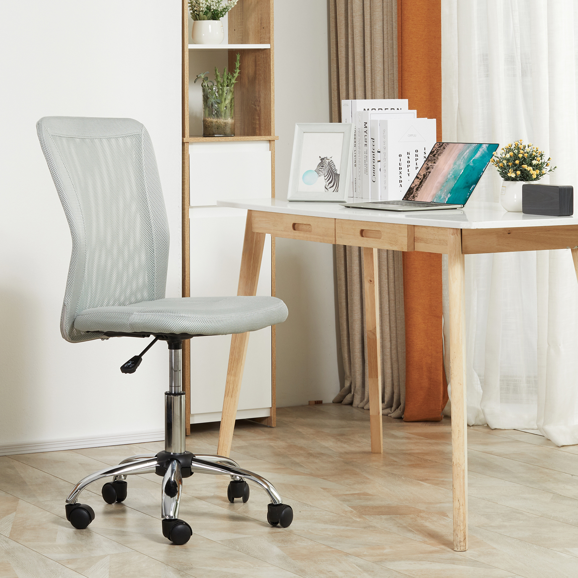Una oficina moderna con una silla de malla gris, un escritorio blanco con una laptop y una estantería blanca al fondo.