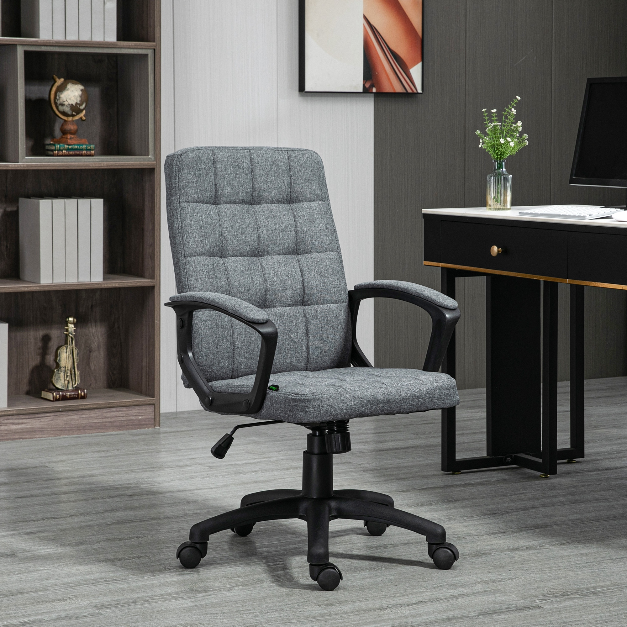 Silla de oficina gris en un entorno de oficina. Apoyabrazos y base negros. Tela gris. Escritorio y estantería al fondo.