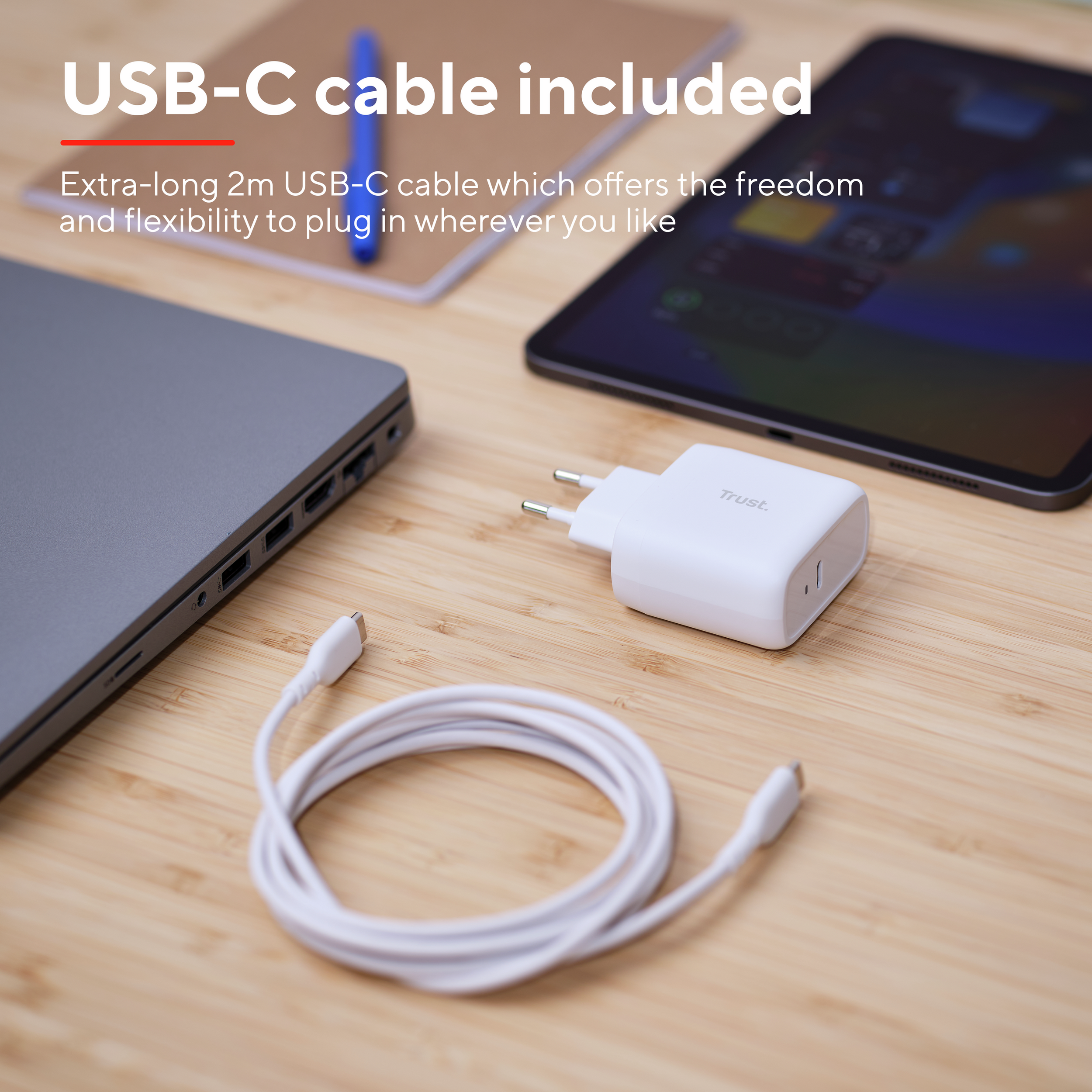 Een witte oplader, een witte kabel, een laptop en een tablet op een houten tafel.