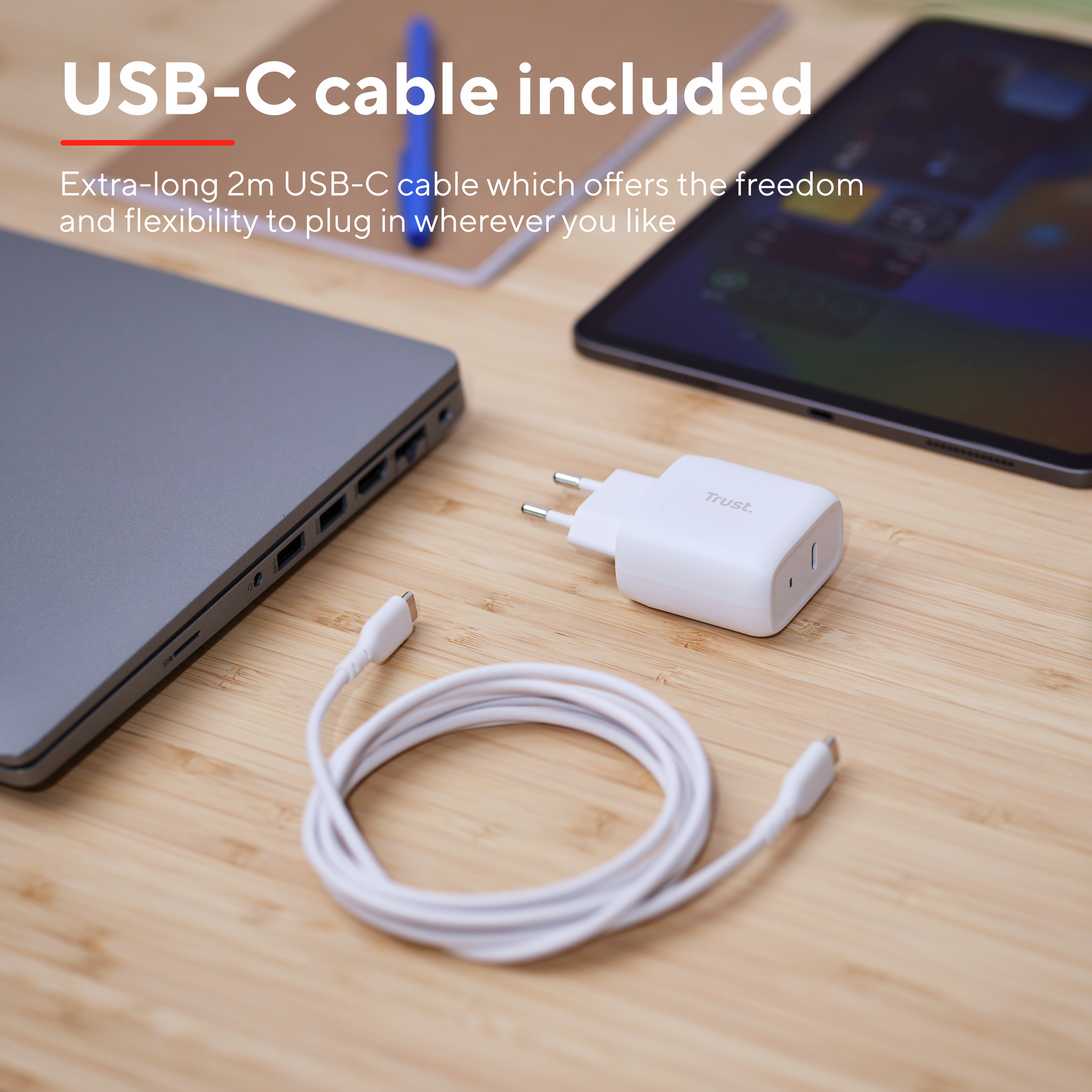USB-C-kabel, oplader en laptop op een houten oppervlak. Een tablet staat op de achtergrond. Tekst: 'USB-C-kabel inbegrepen'.