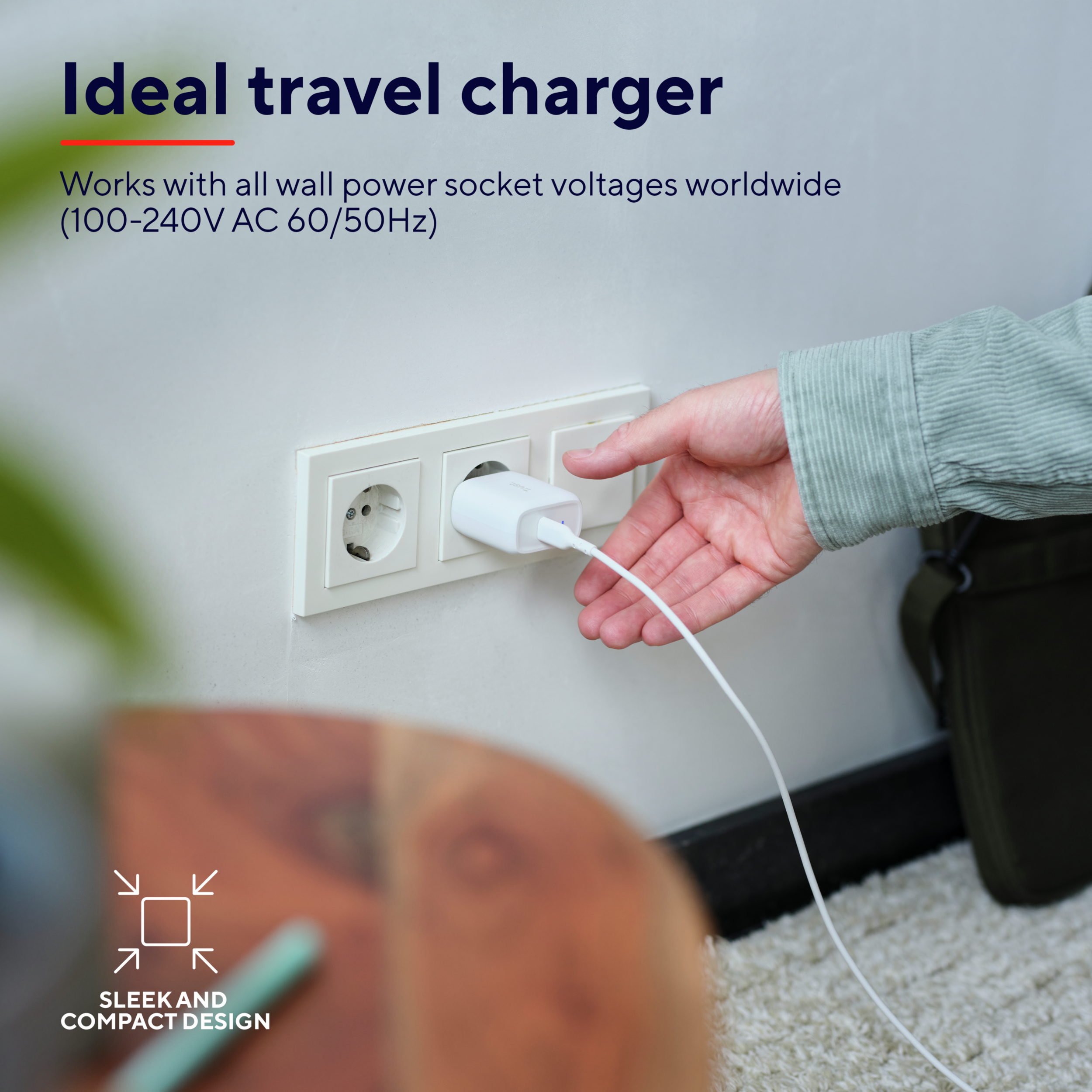 Een hand die een witte oplader in een stopcontact steekt. De tekst zegt "Ideal travel charger".