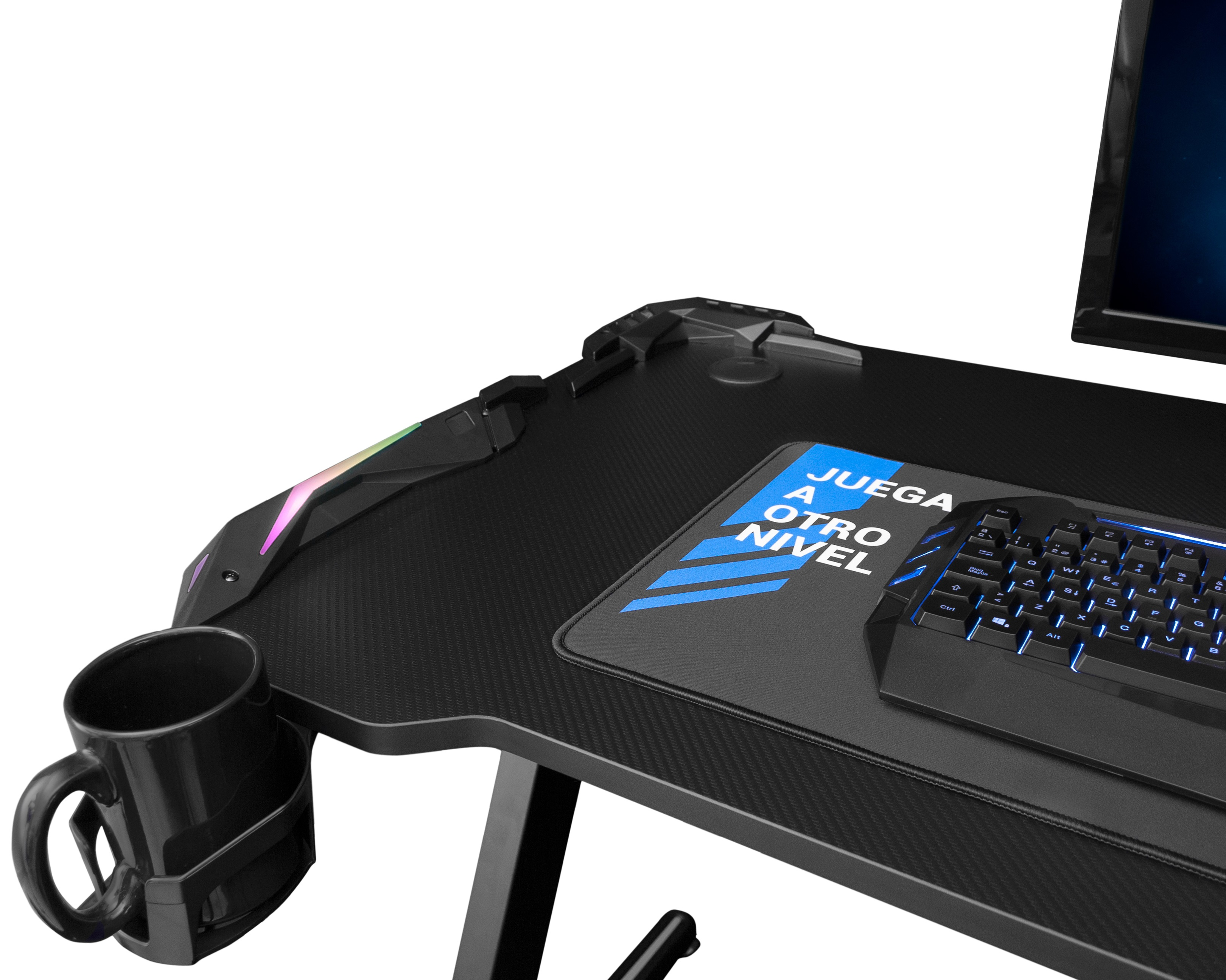 Escritorio negro para juegos con teclado, alfombrilla y taza. Un monitor es visible en el fondo.