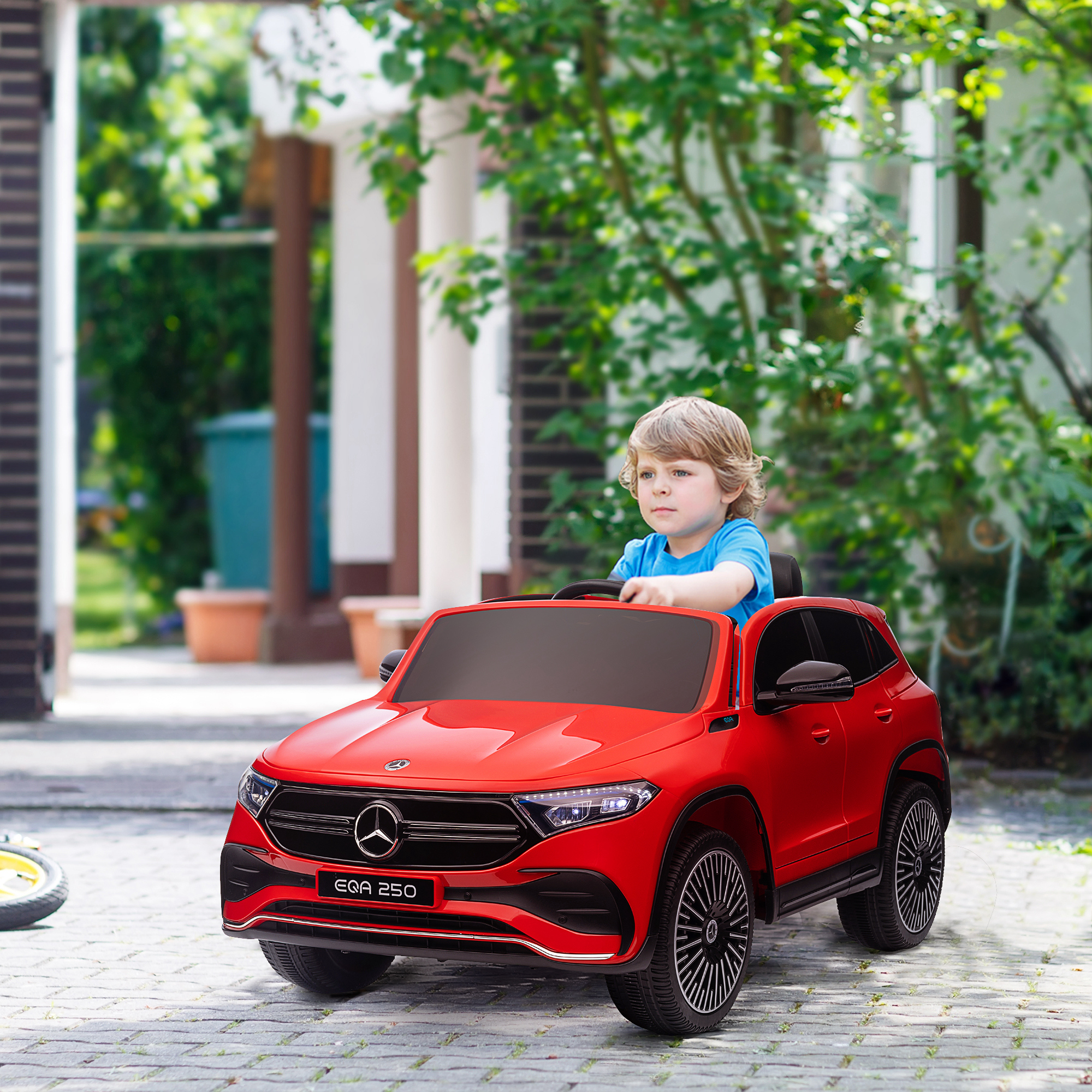 Un'auto giocattolo rossa con un bambino dentro. Lo sfondo è una casa e degli alberi.