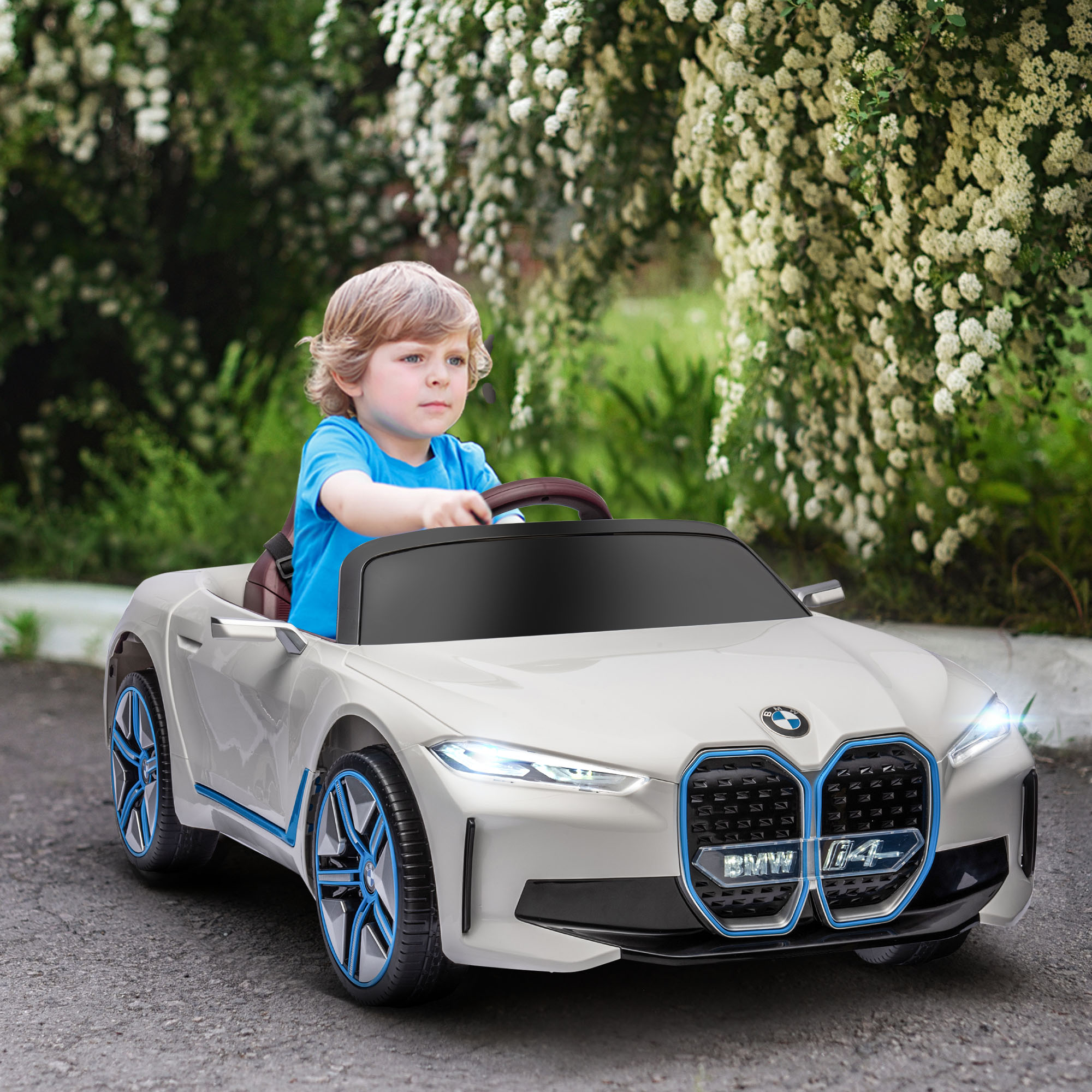 Un bambino piccolo che guida un'auto giocattolo bianca. È visibile uno sfondo verde di piante.