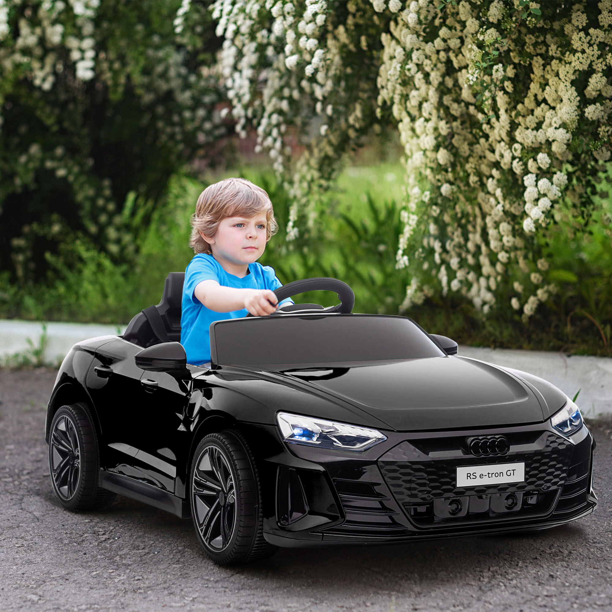 Un niño sentado en un coche de juguete negro en un camino pavimentado cerca de vegetación.