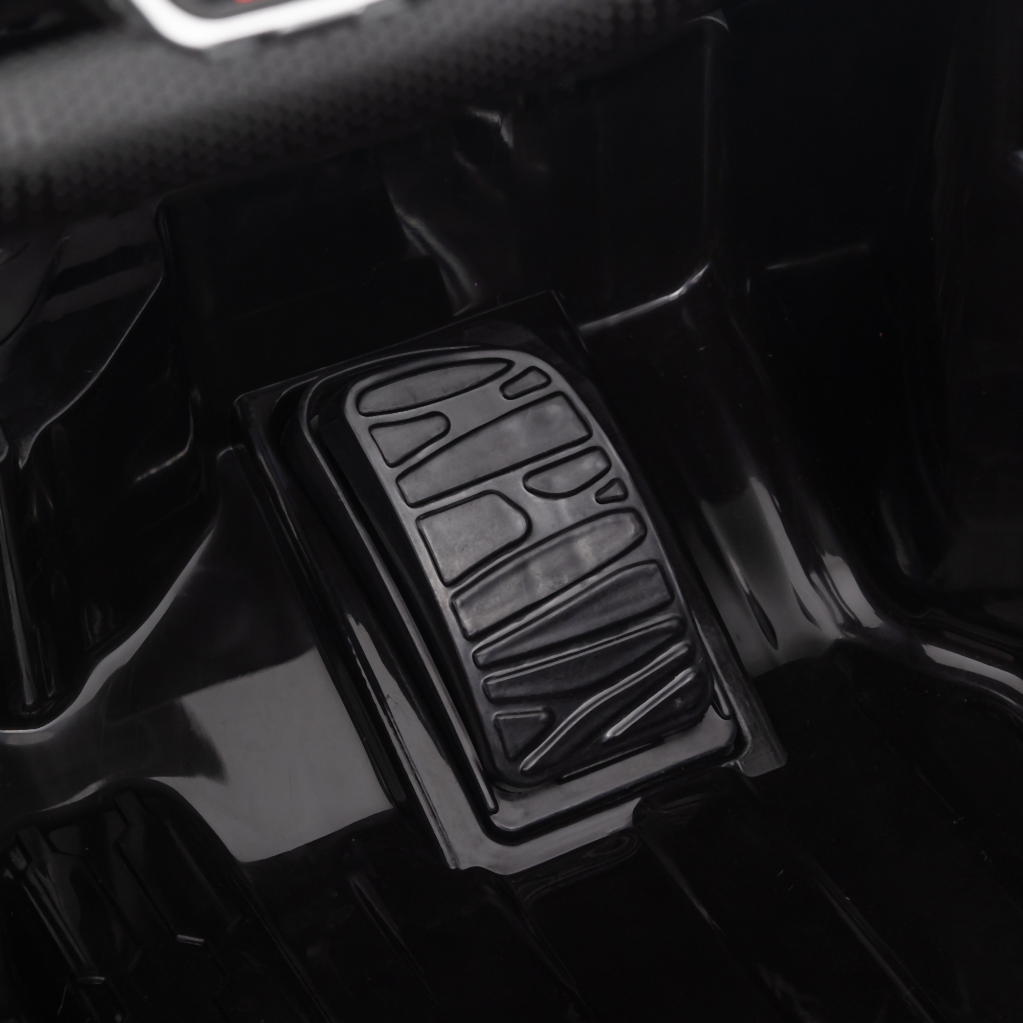 Pedale di un'auto giocattolo. Plastica nera. Sfondo nero.