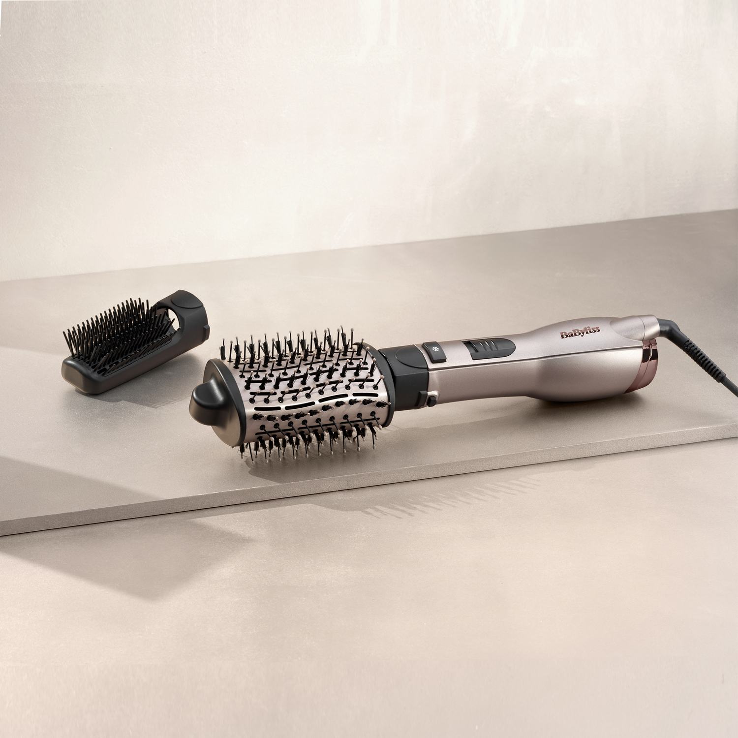 Un fer à friser argenté avec brosse noire et un accessoire de brosse séparé.