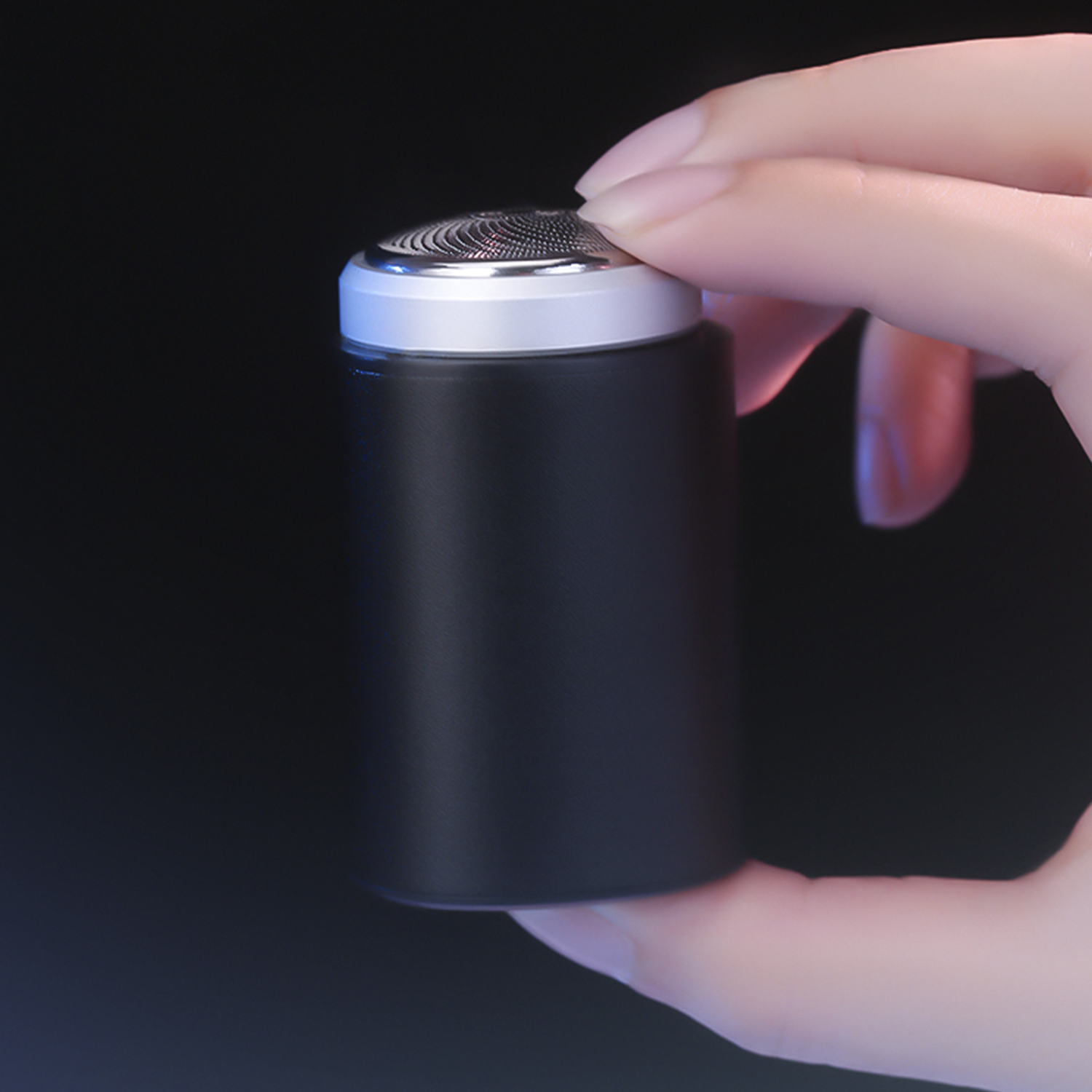 Eine Hand hält einen schwarzen und silbernen Elektrorasierer. Der Hintergrund ist dunkel.