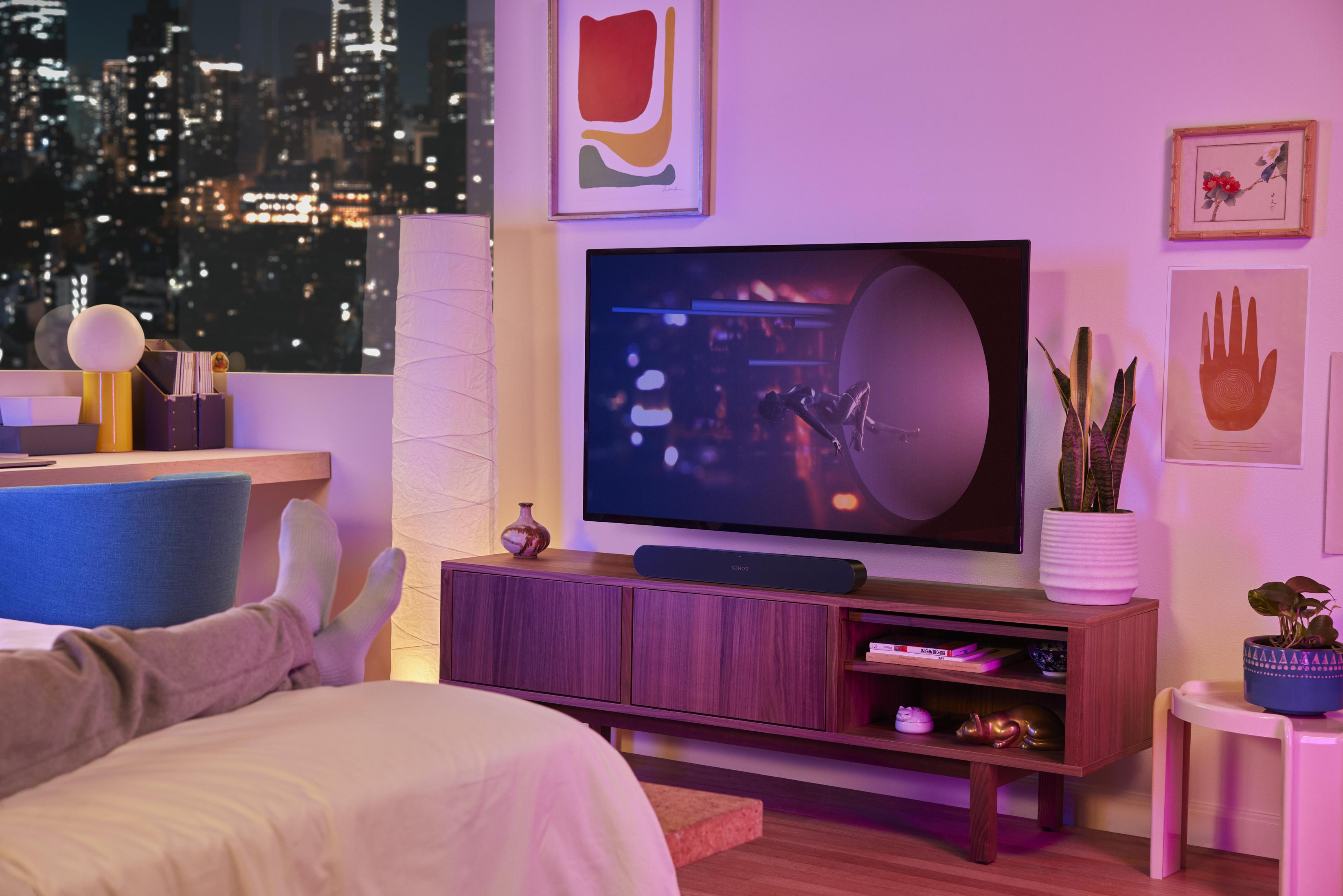 Wohnzimmer bei Nacht mit Fernseher, Soundbar und einer Person mit hochgelegten Füßen auf einem Bett.
