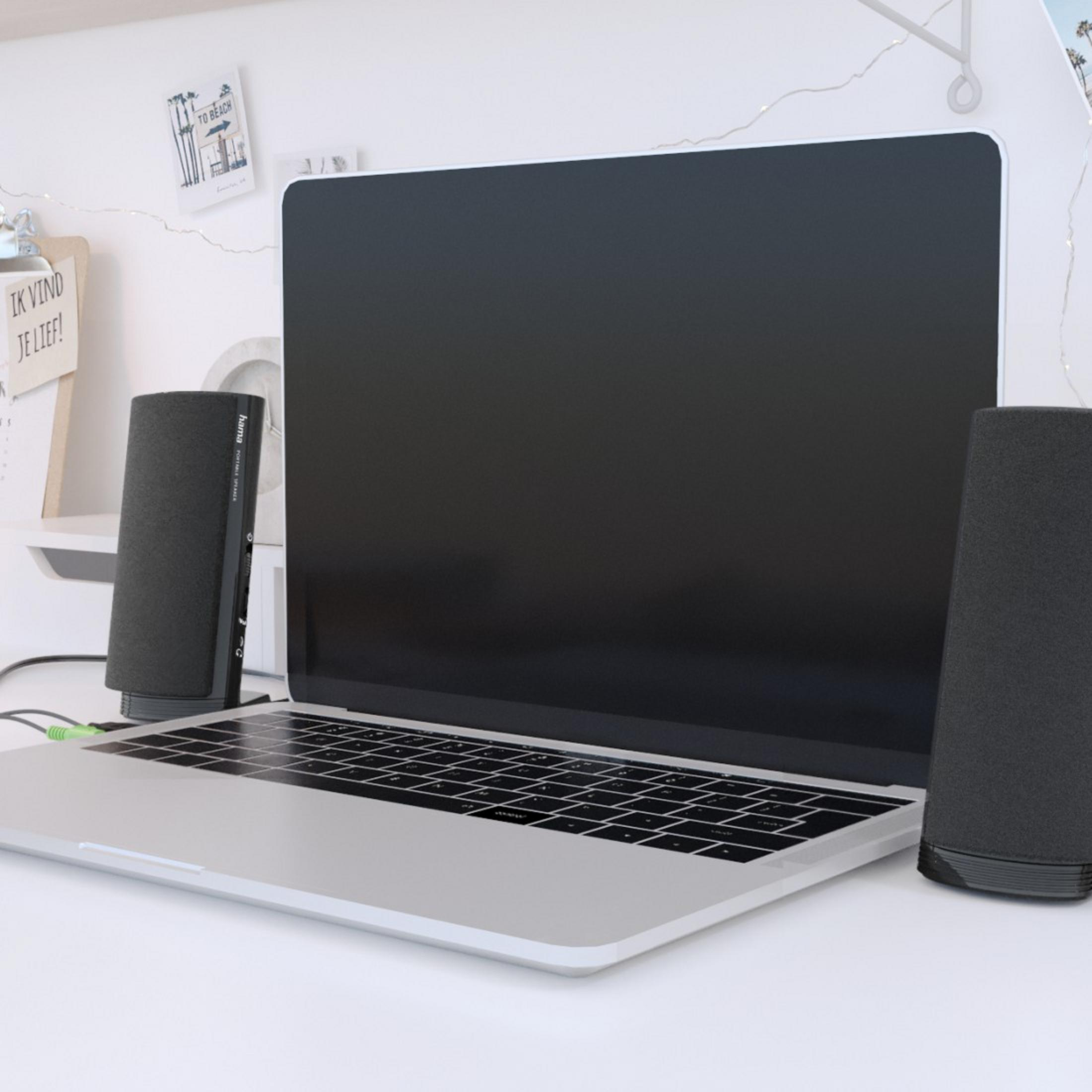 Laptop mit schwarzem Bildschirm, zwei schwarzen Lautsprechern und einem weißen Schreibtisch mit ein paar Gegenständen.
