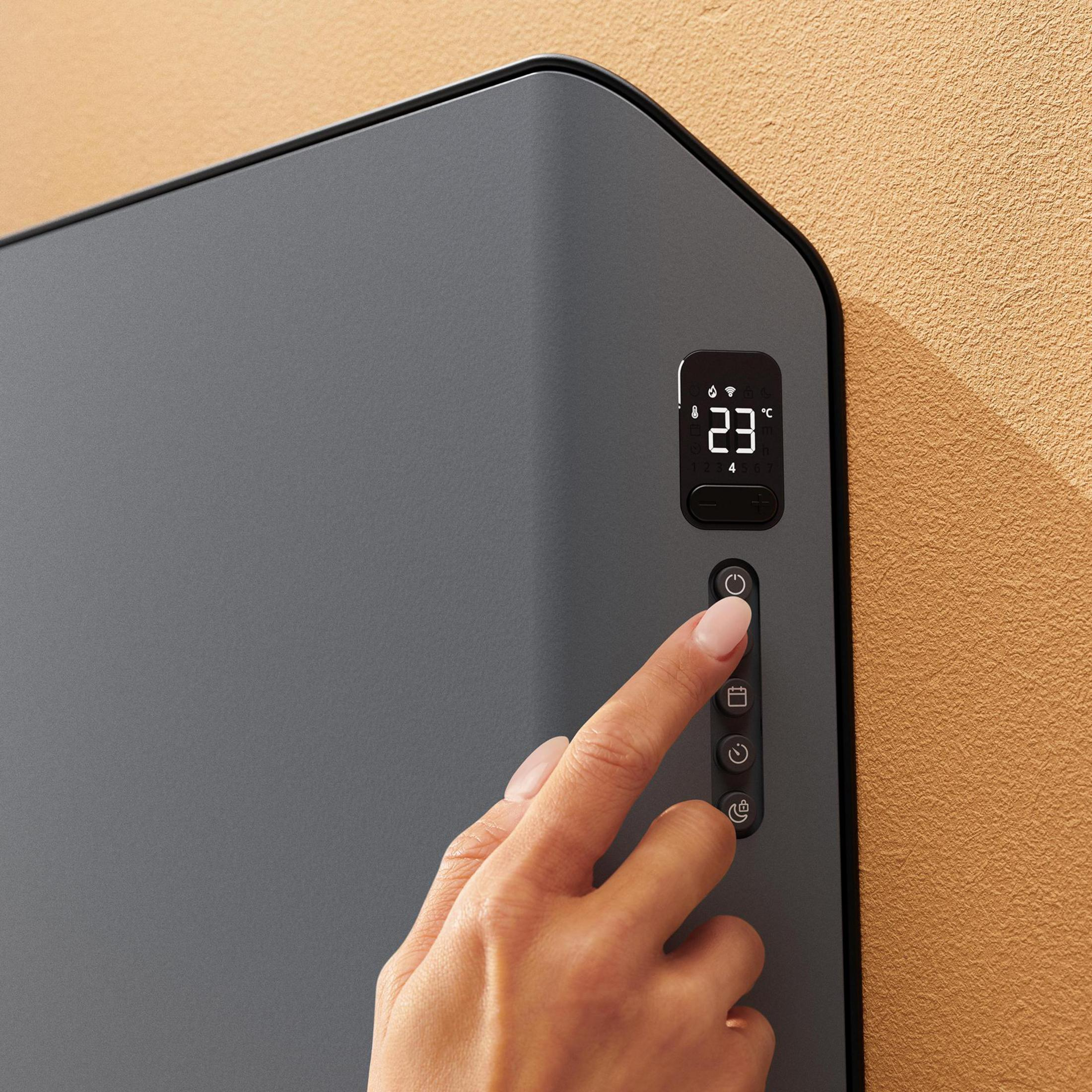 Dłoń dotykająca panelu sterowania inteligentnego grzejnika na ścianie.