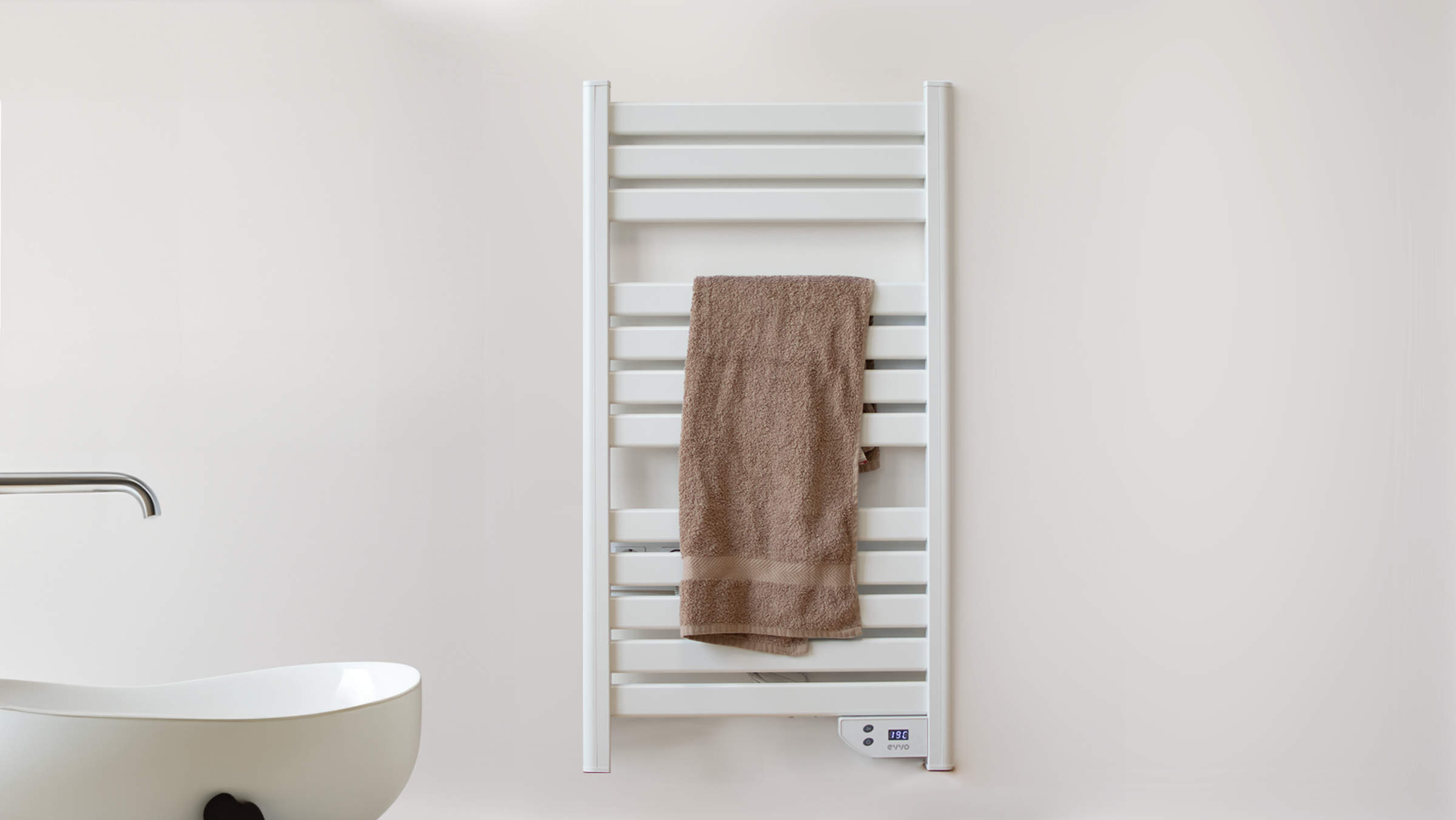 Un toallero blanco y rectangular con una toalla marrón colgada frente a una pared blanca.