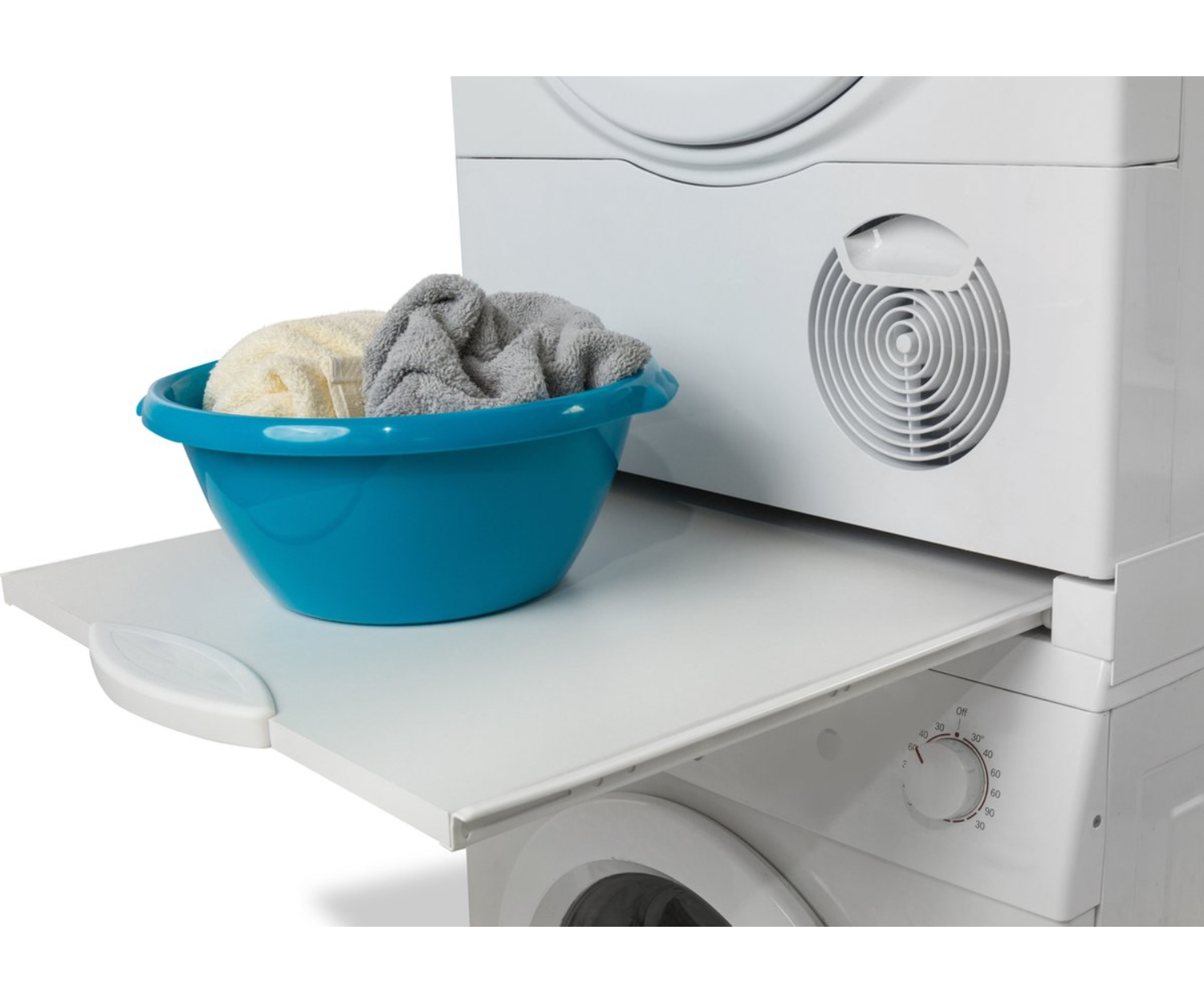 Stacked white washing machine and dryer with a white pull-out shelf. A blue bowl with towels sits on shelf.
