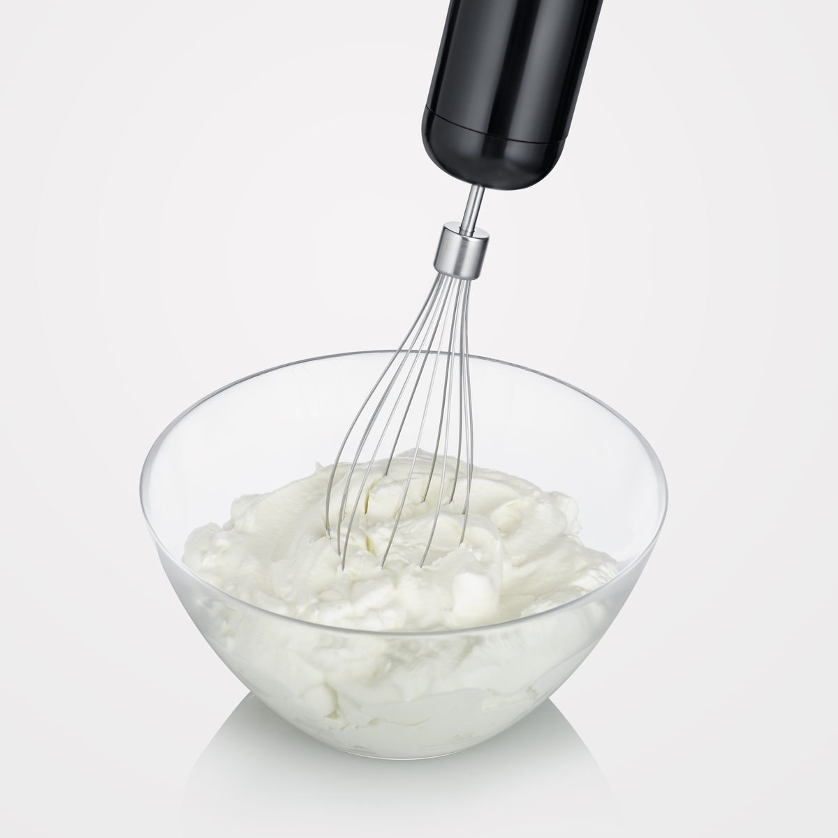 Handmixer die room in een glazen kom klopt. Zwarte mixer, witte achtergrond.