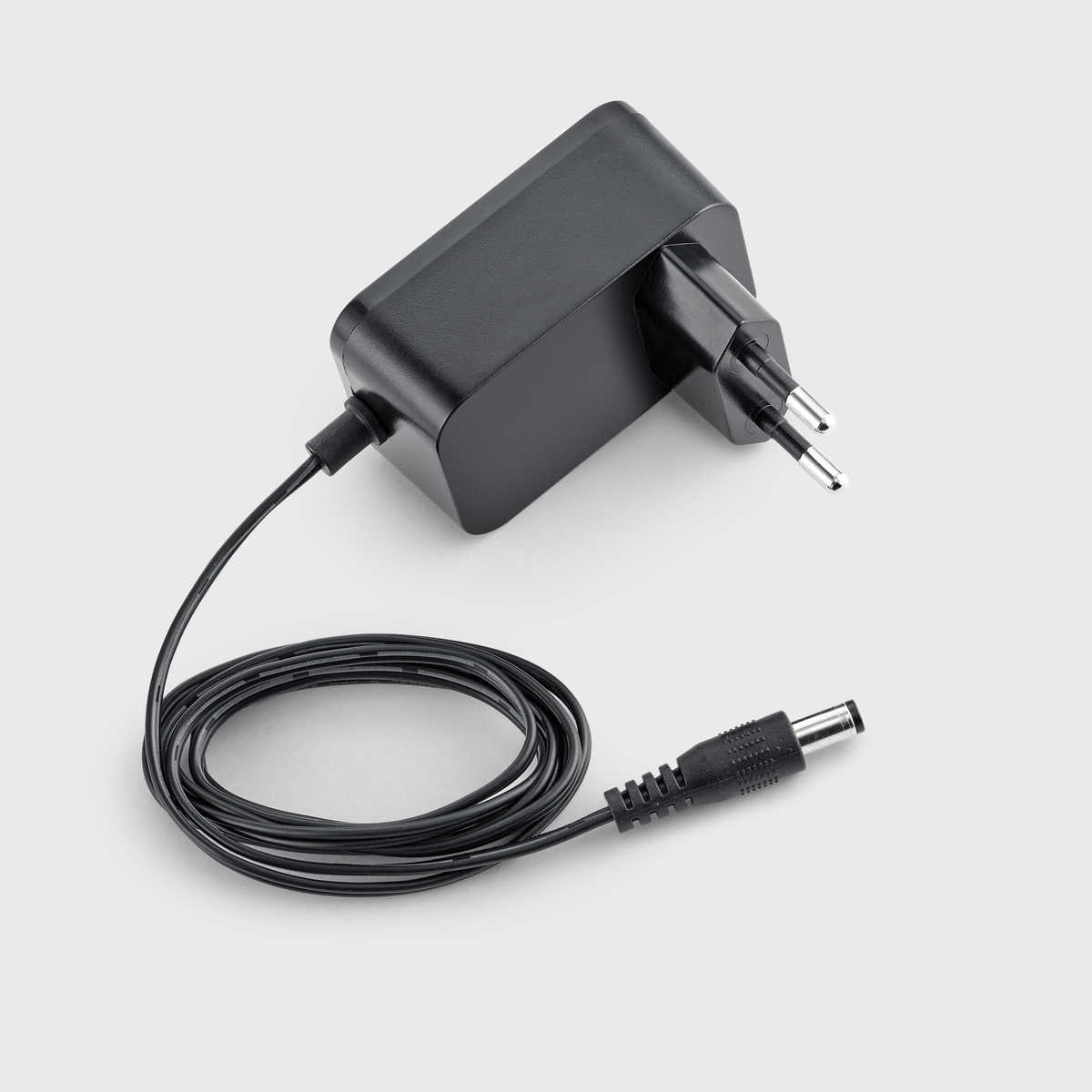 Een zwarte voedingsadapter met een zwarte kabel en stekker op een lichtgrijze achtergrond.