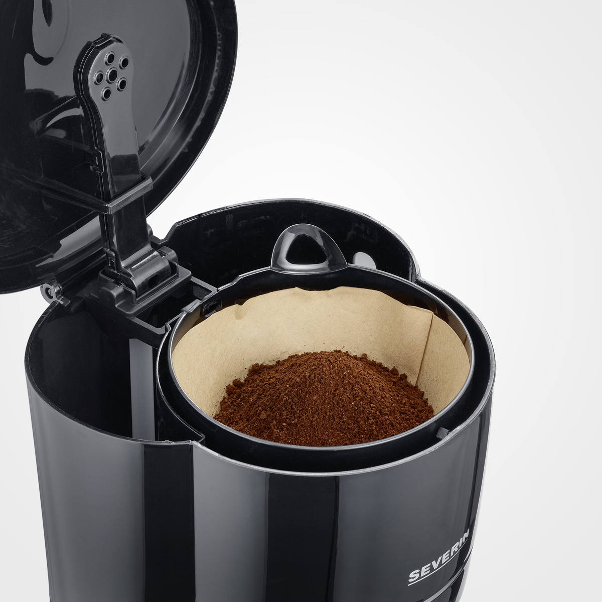 A black coffee maker with a filter filled with coffee grounds. Coffee machine open.
