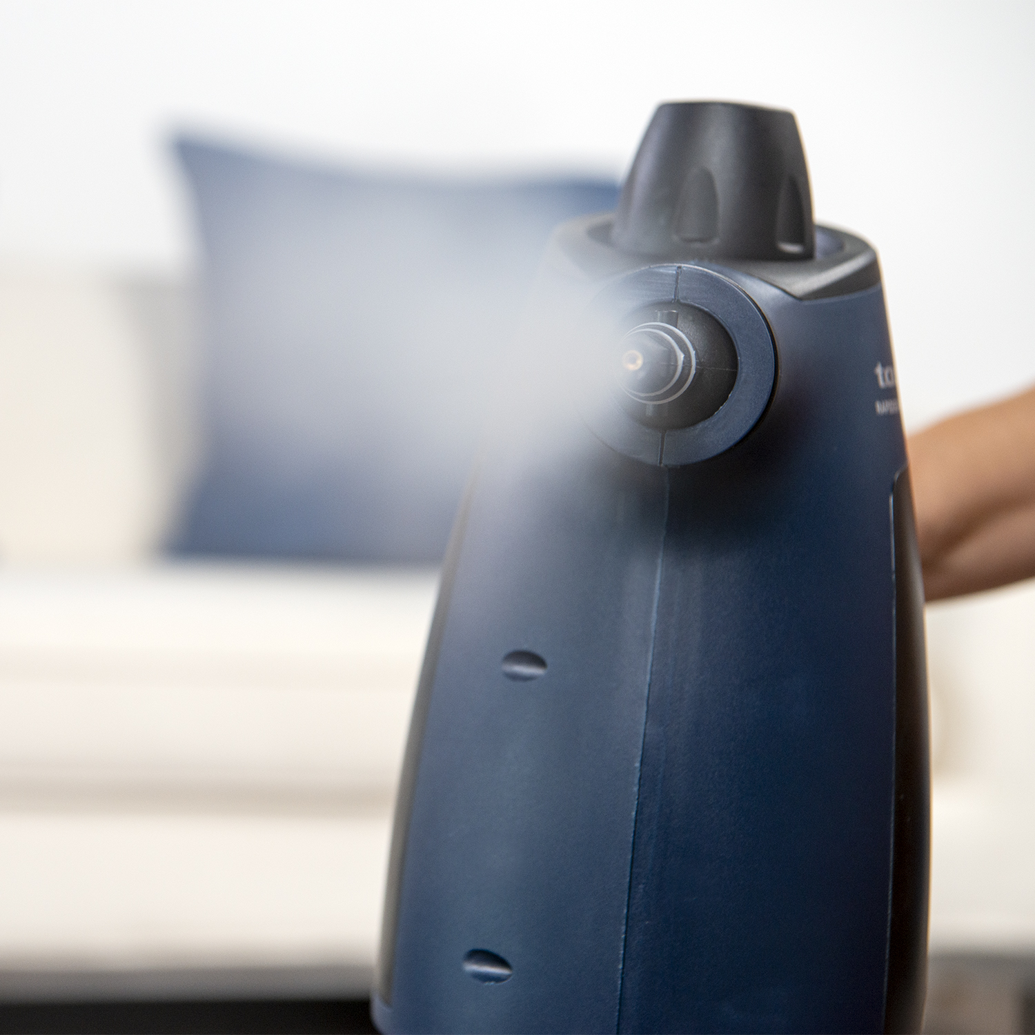 Granatowa myjka parowa, z wydobywającą się parą. W tle niebieska poduszka.