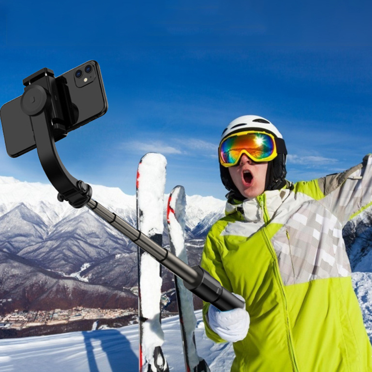 Skifahrer mit Selfie-Stick, Skiausrüstung, schneebedeckte Berge, klarer blauer Himmel.