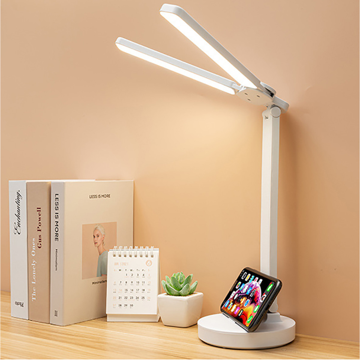 Eine weiße Schreibtischlampe mit zwei Lichtern, Telefon auf Ständer, Bücher und ein Kalender.