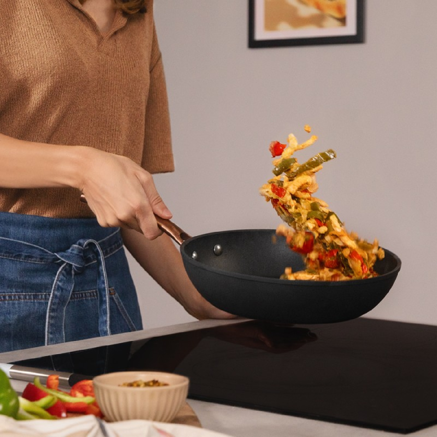 Osoba wyrzuca jedzenie z czarnej patelni. Warzywa w powietrzu.