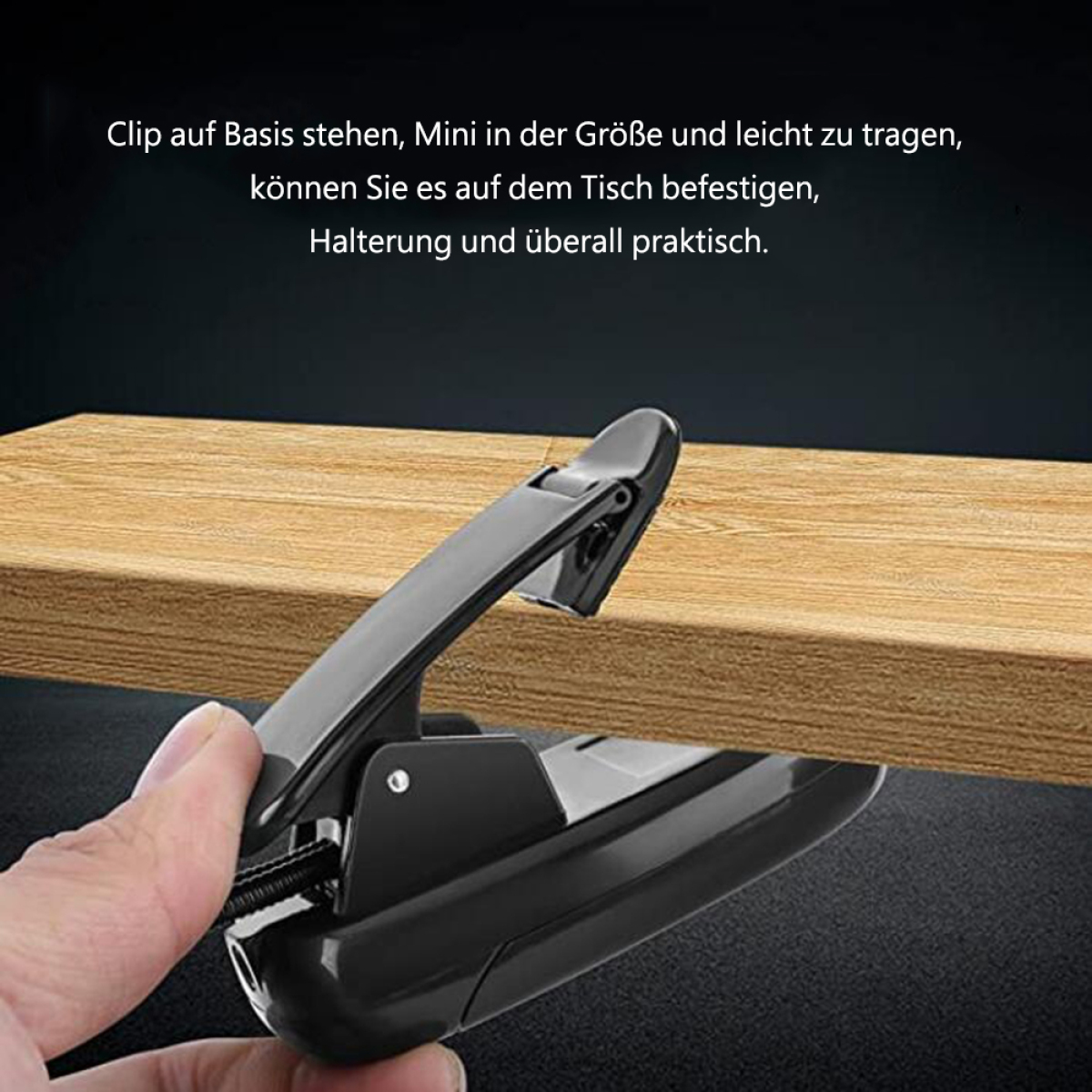Eine Hand hält einen schwarzen Clip neben einem Holztisch. Der Clip ist für Papiere gedacht.