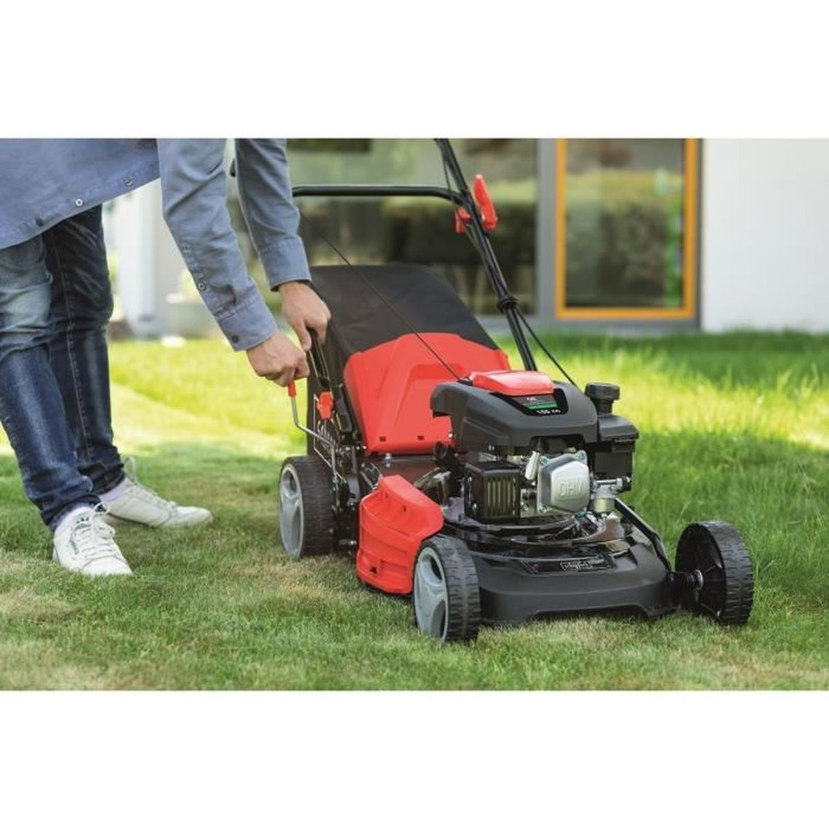 Man start een rood-zwarte grasmaaier op gras.