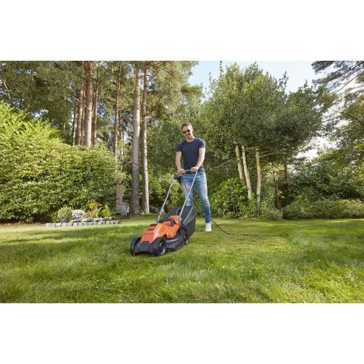 Ein Mann mäht Rasen mit einem orange-schwarzen Rasenmäher in einem Garten mit Bäumen.