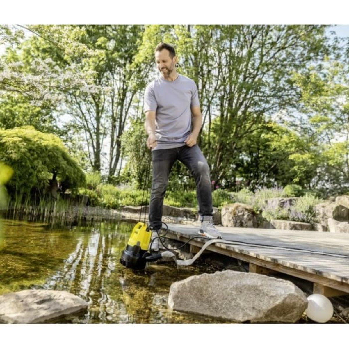 Mężczyzna używa żółto-czarnej pompy w stawie. Drzewa i skały w tle.