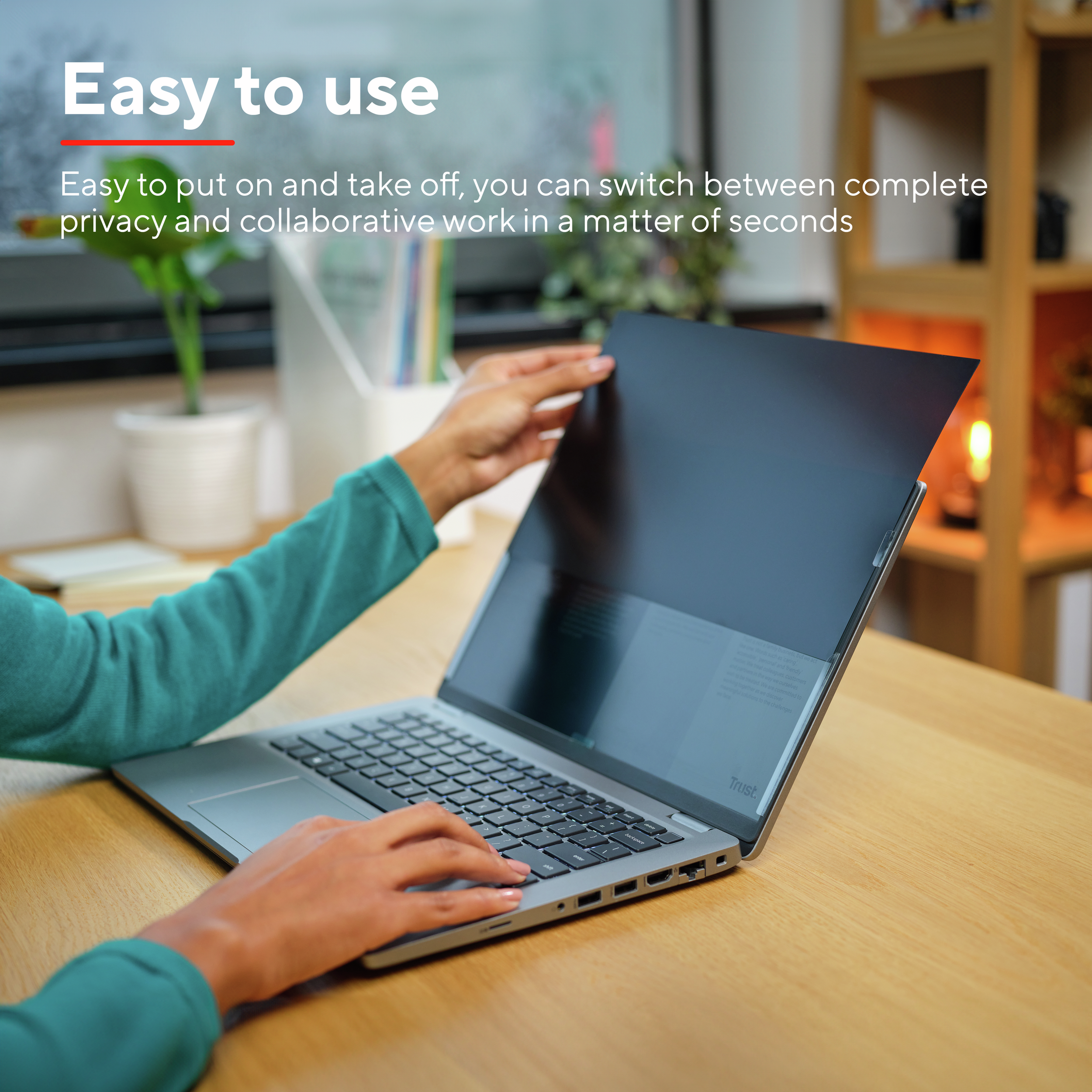Persona che utilizza un laptop con schermo per la privacy. Scrivania in legno con lampada.