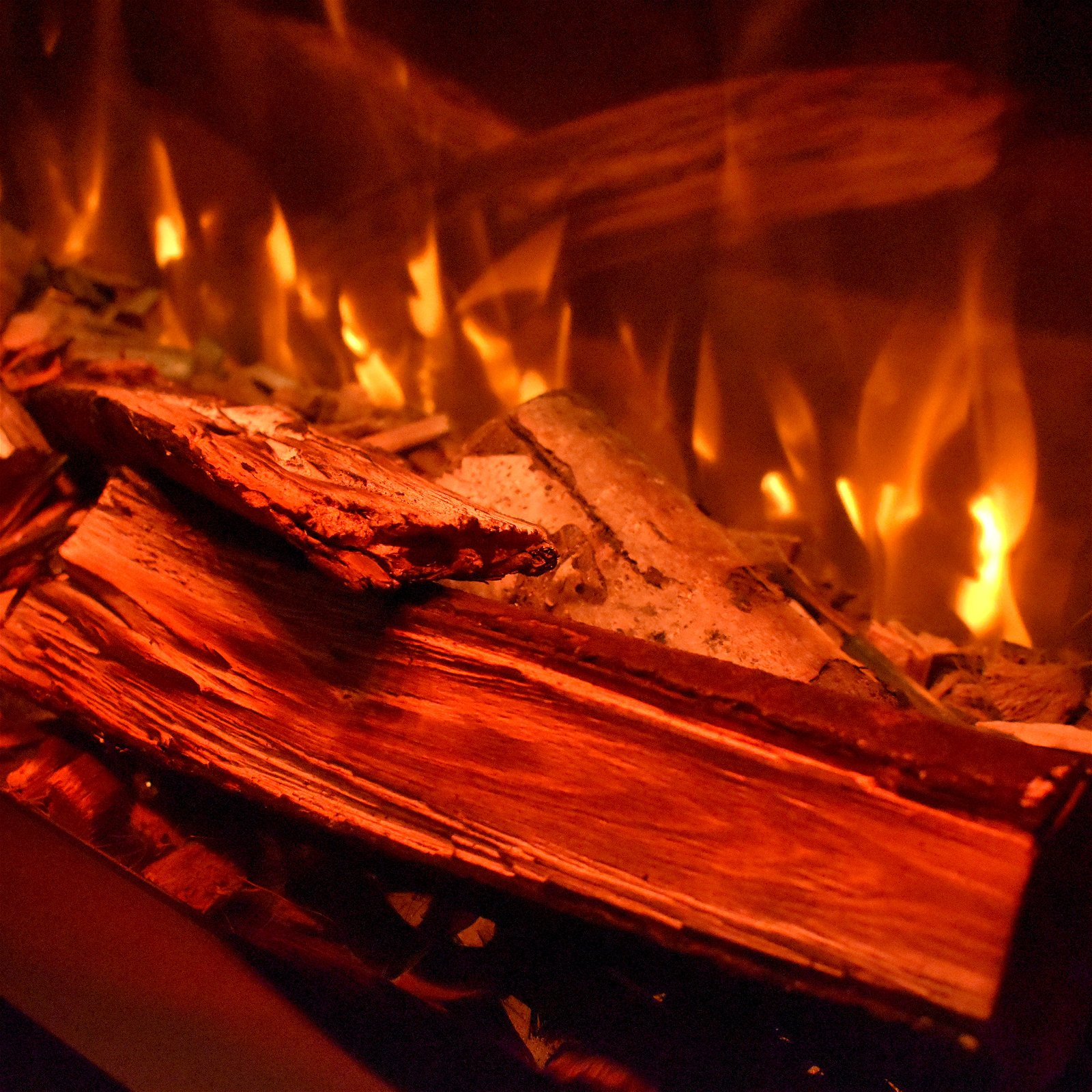 Kamin mit brennenden Holzscheiten, Flammen und Holzstruktur.