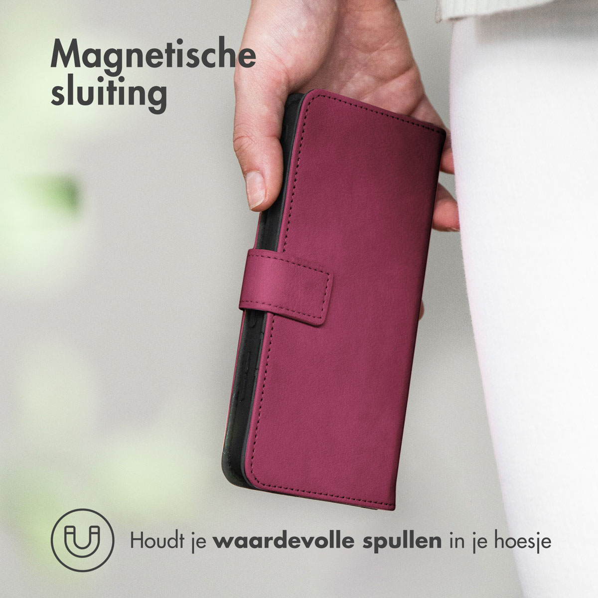 Een bordeauxrode telefoonhoes. De hoes is gesloten, met een magnetische sluiting, en wordt door een hand vastgehouden.