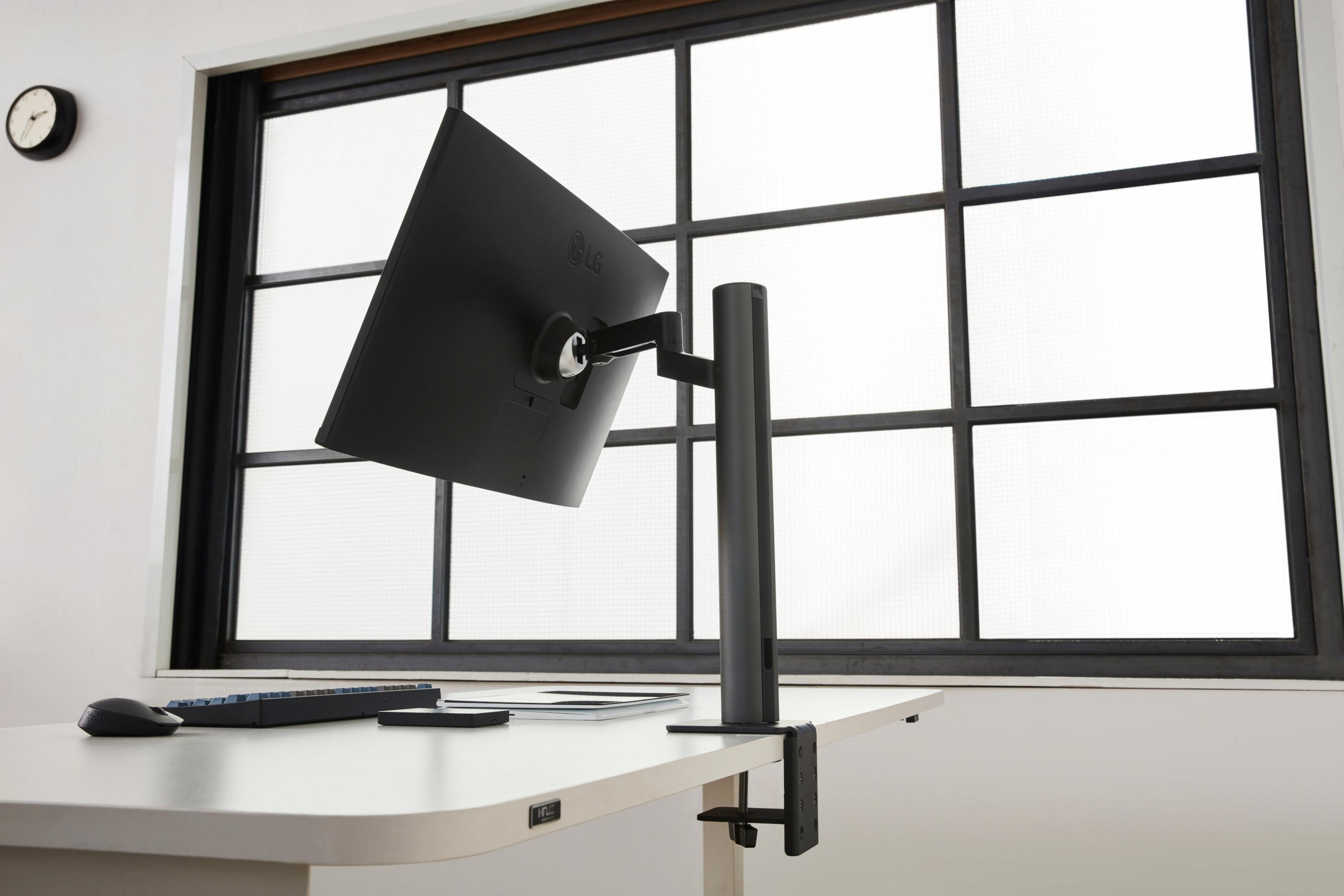 Ein Computermonitor auf einem Schreibtisch. Der Monitor ist abgewinkelt. Ein Fenster befindet sich im Hintergrund.