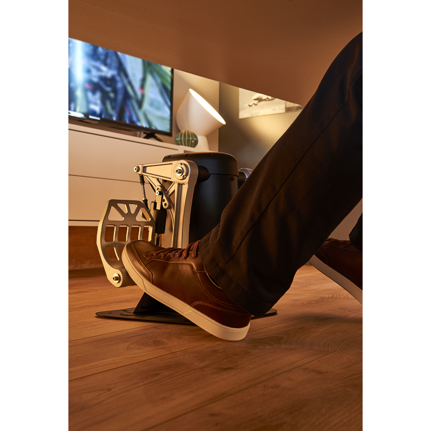 I piedi di una persona con scarpe marroni che premono i pedali di gioco, sotto una scrivania.
