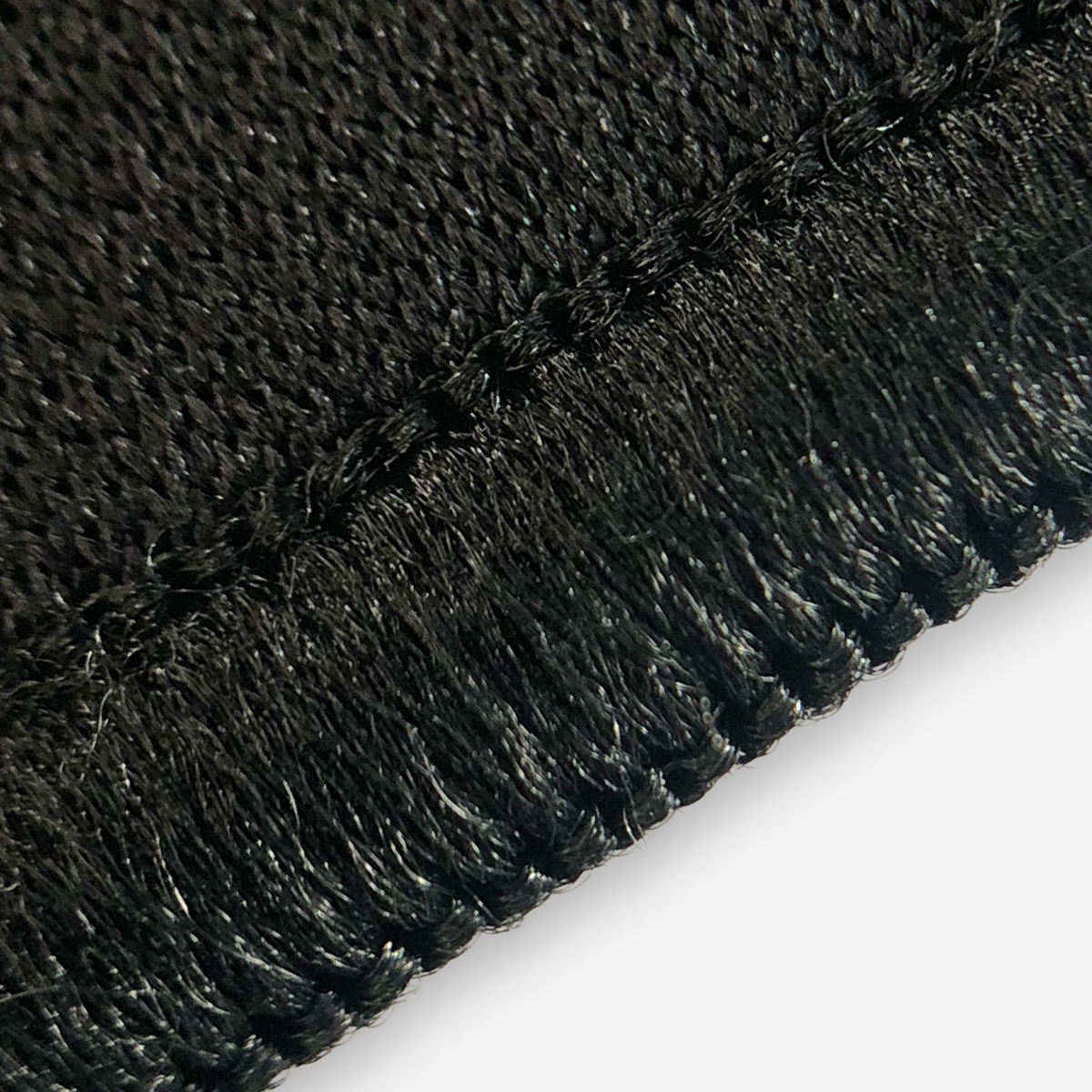 Close-up van zwarte stof met zichtbare stiksels en textuur, tegen witte achtergrond.