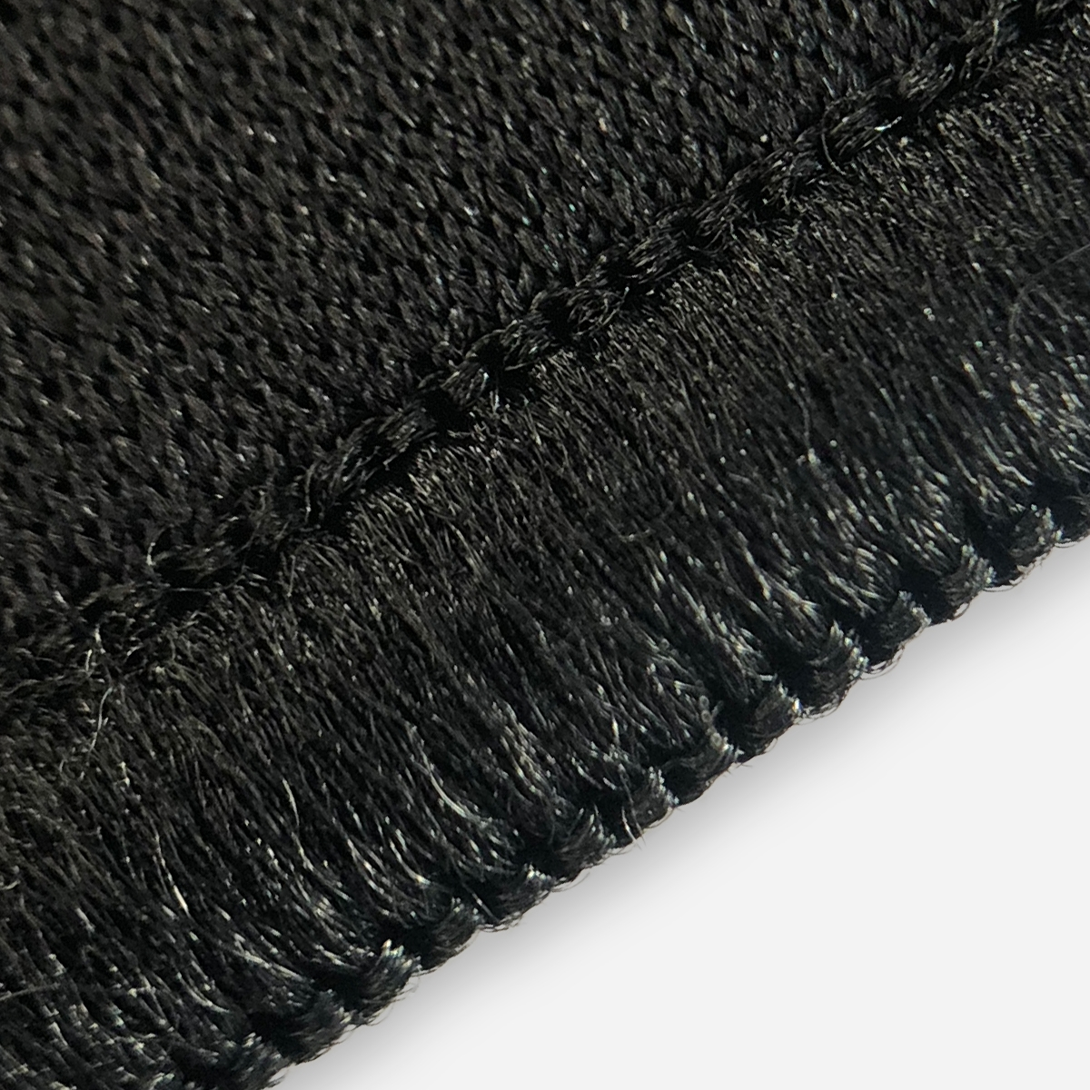 Detalle de tela negra, texturizada con costuras. Fondo blanco.