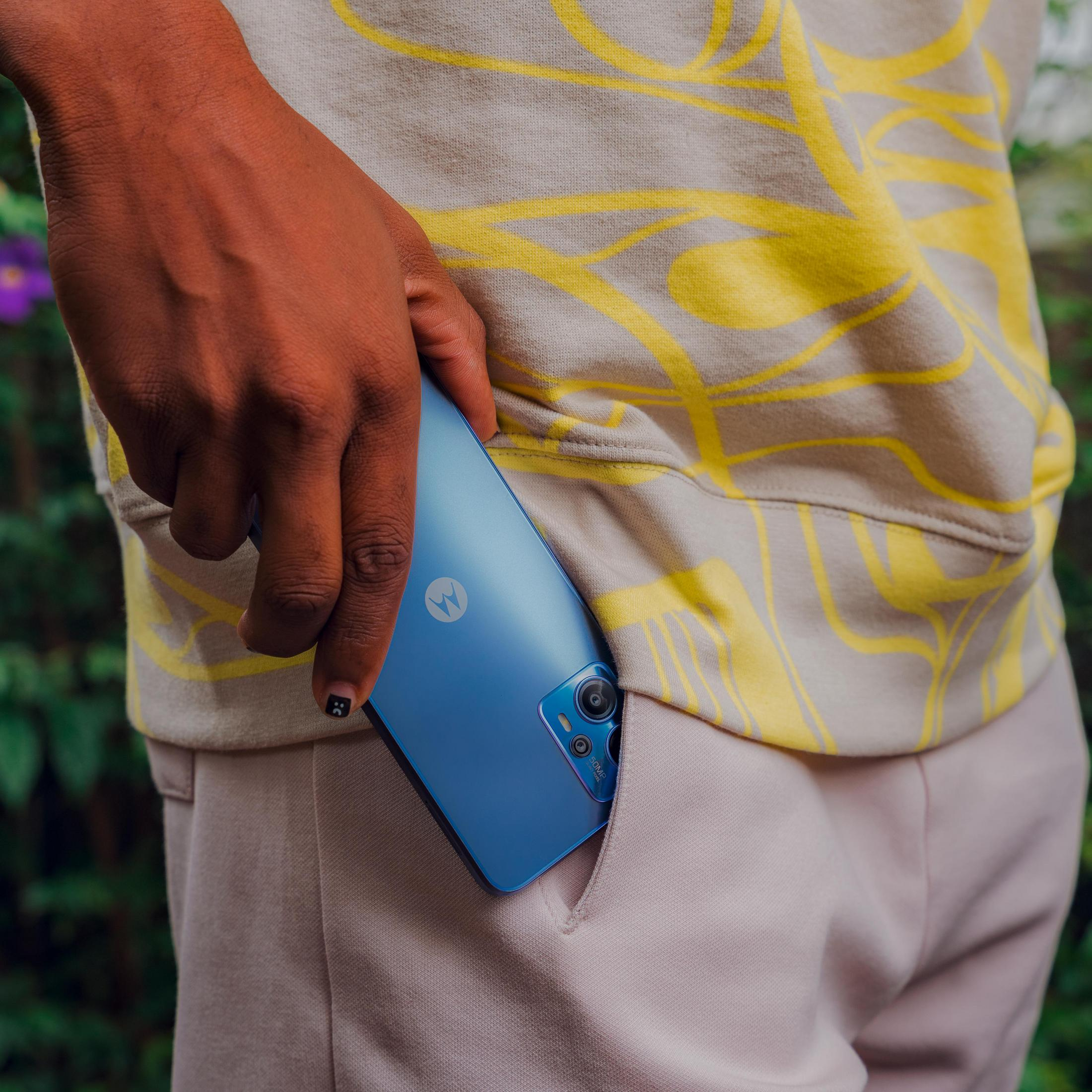 Osoba trzymająca niebieski telefon w kieszeni. Osoba ma na sobie beżową bluzę.