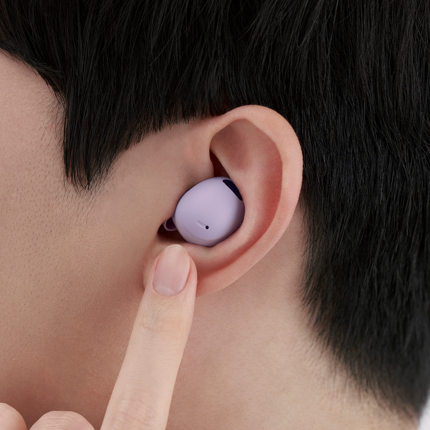 Ucho osoby z włożoną fioletową słuchawką i palcem wskazującym.