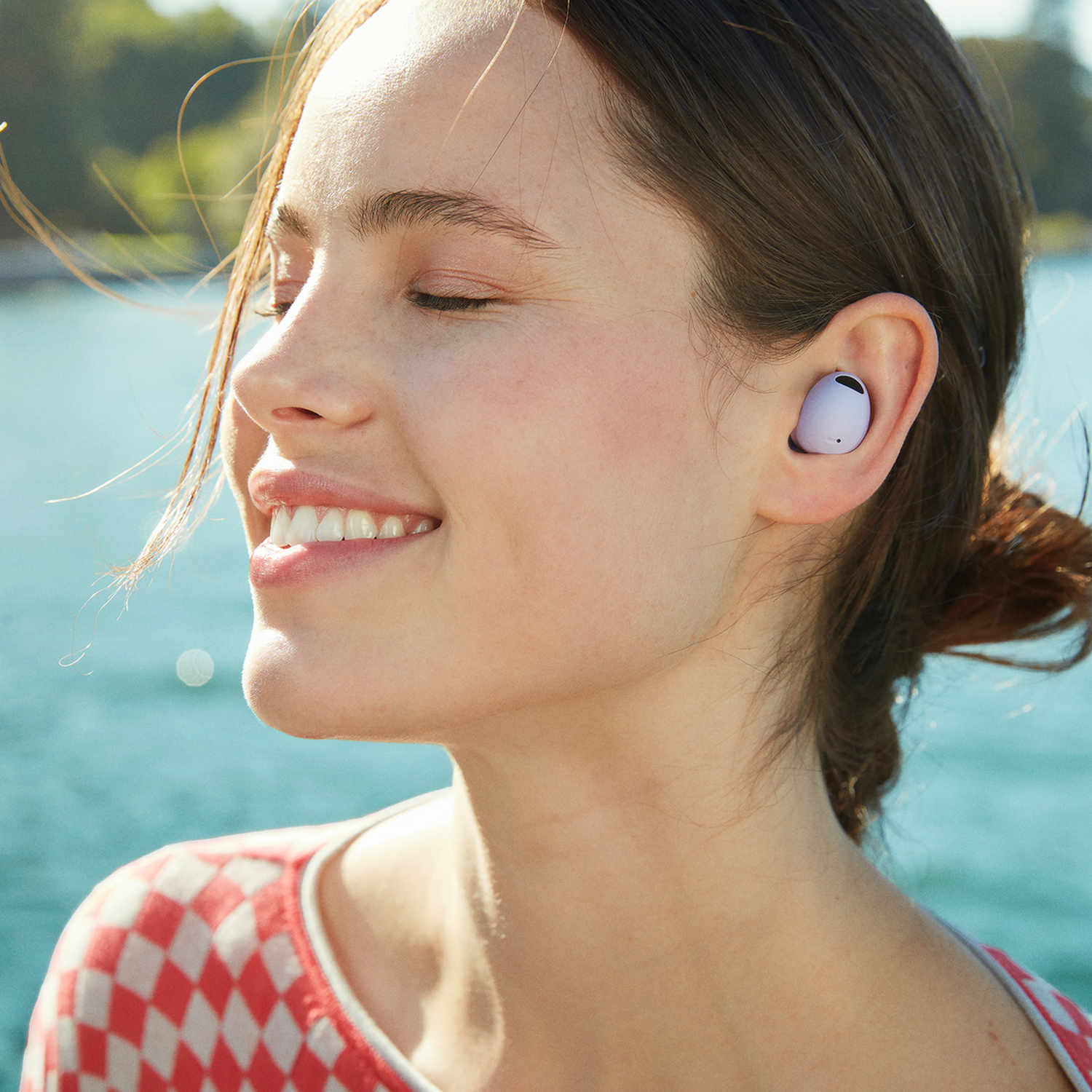 Kobieta ze słuchawkami w uchu, uśmiechnięta, z niebieskim tłem wody.