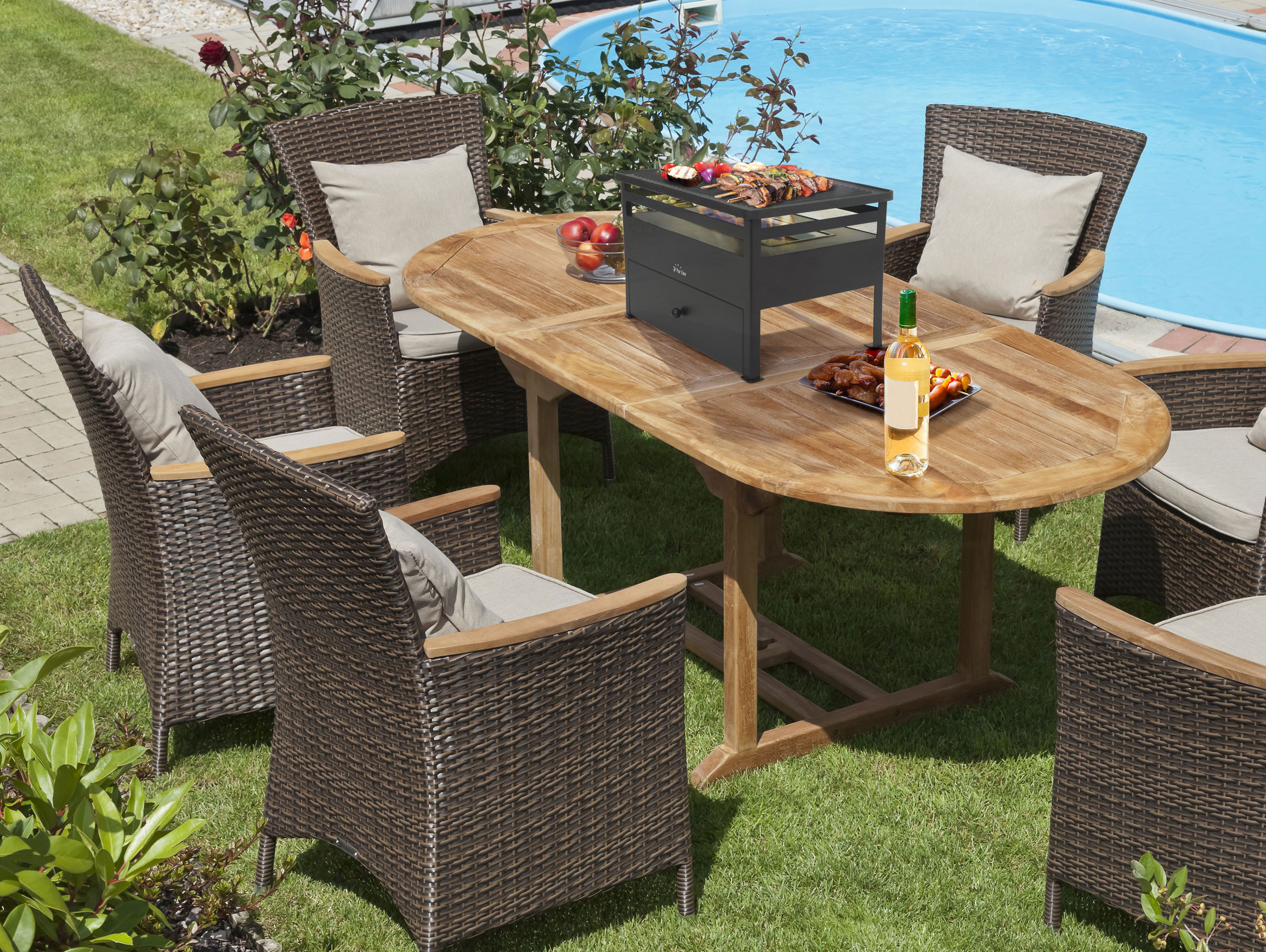 Esstisch im Freien mit Stühlen, Grill, Essen und Wein am Pool. Grünes Gras und Pflanzen sind drum herum.