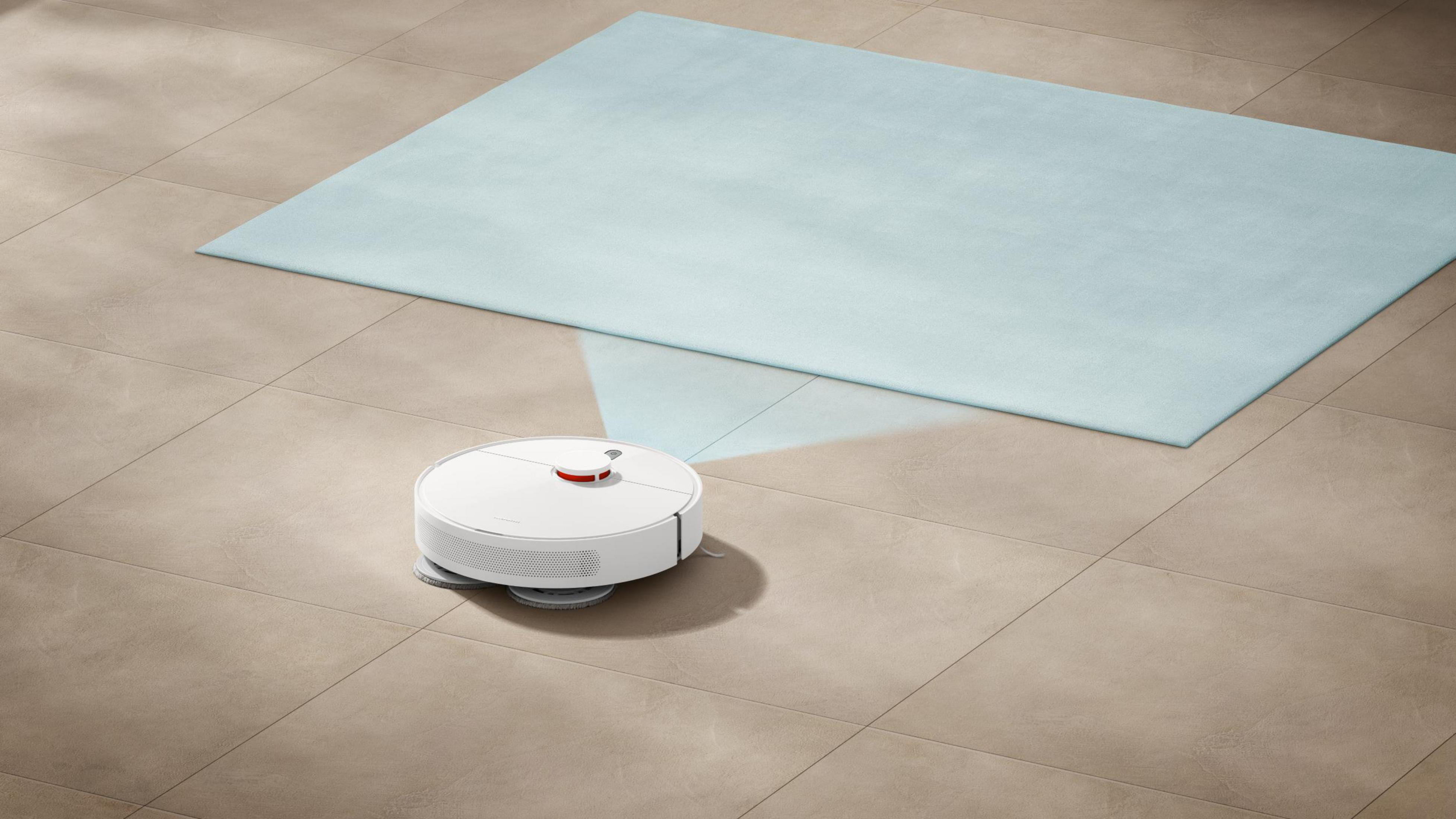 Açık mavi bir halıyla fayans bir zeminde beyaz bir robot süpürge. Robot ortada.