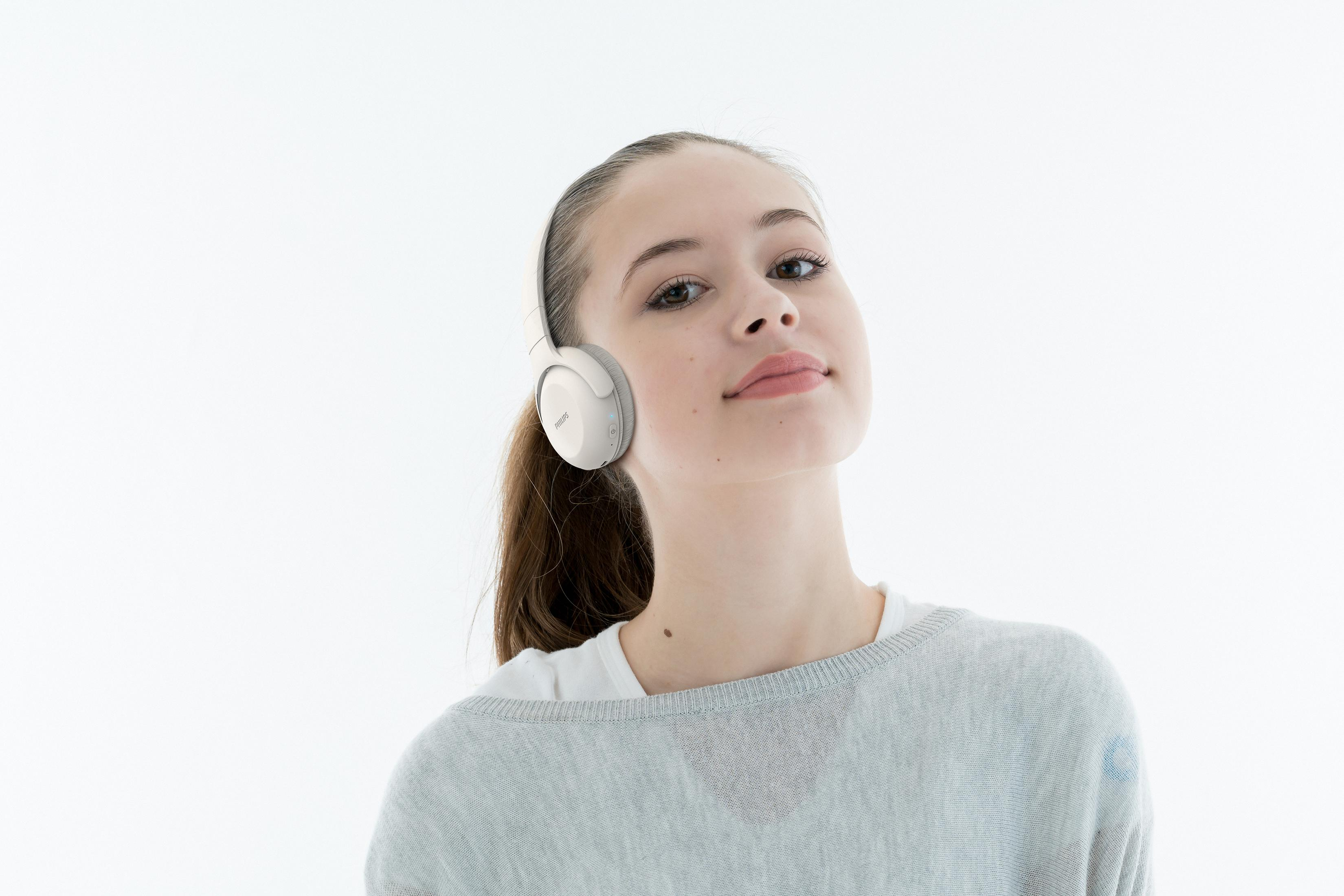 Mujer joven con auriculares blancos y coleta. Fondo blanco, sonriendo, mirando a la cámara.